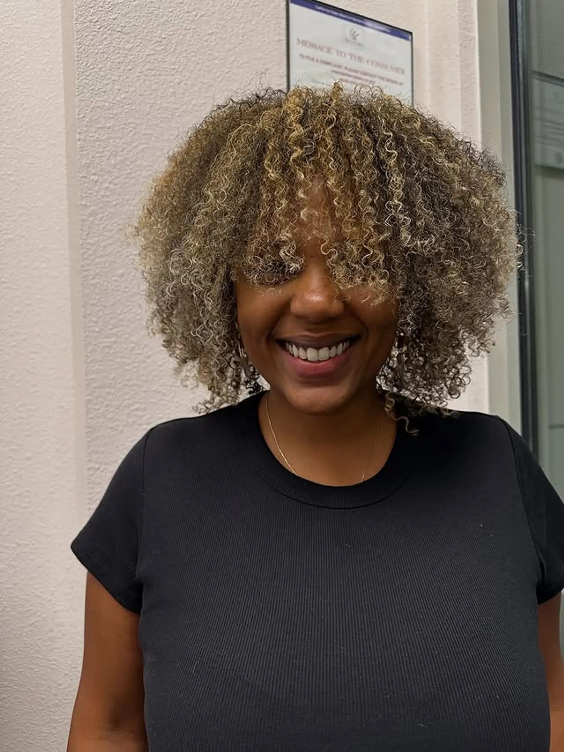 A medium-length curly afro with face-framing bangs and blonde highlights. 1