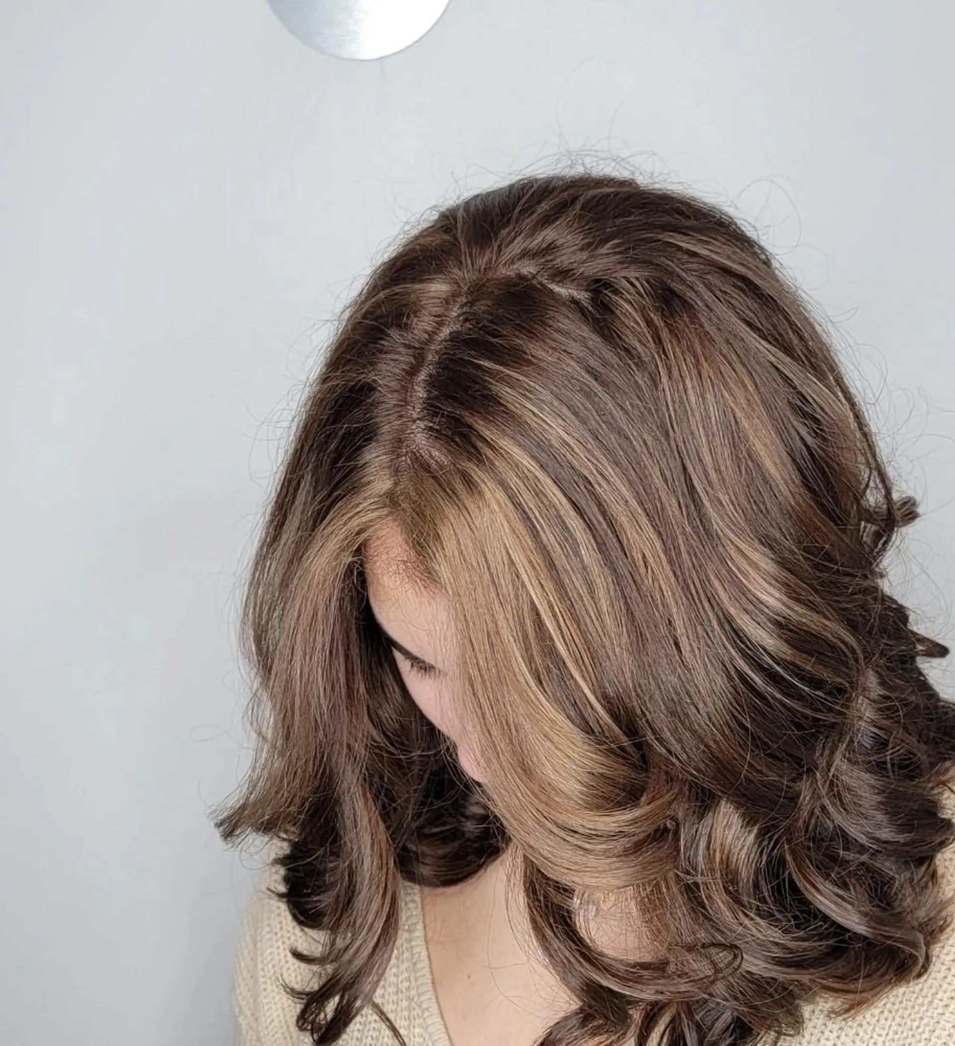Medium-length, wavy hair with chocolate brown base color and honey blonde highlights, styled with soft curls and a middle part, enhanced by a natural shine. 2