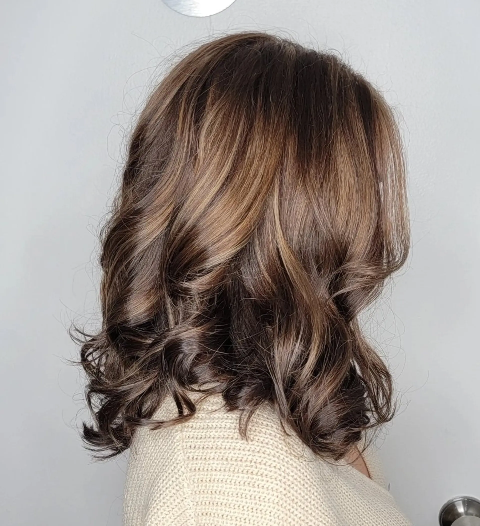 Medium-length, wavy hair with chocolate brown base color and honey blonde highlights, styled with soft curls and a middle part, enhanced by a natural shine. 3