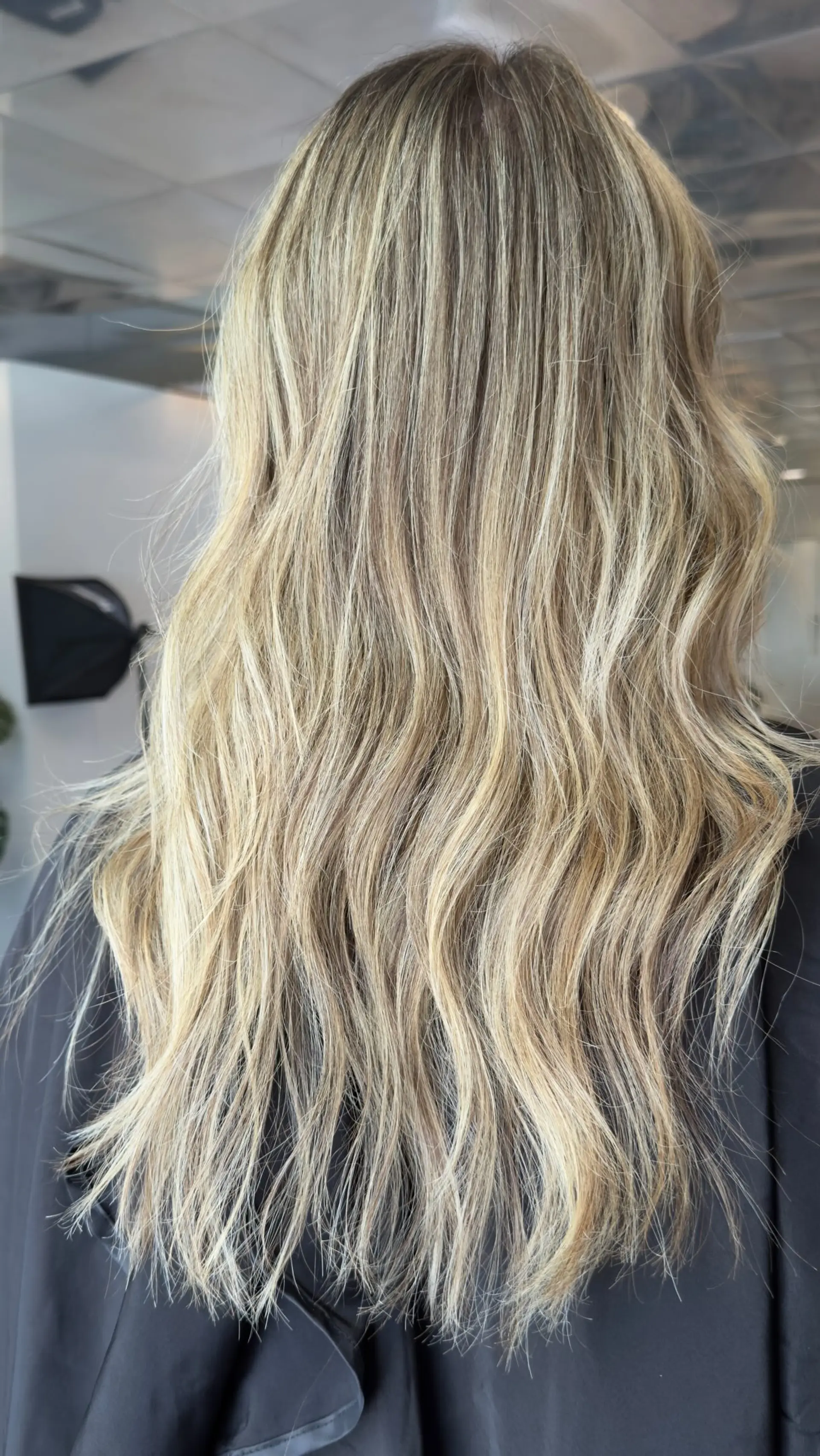 Long hair styled with soft, lived-in waves featuring multi-tonal cashmere blonde highlights blended over a natural light brown base. 1
