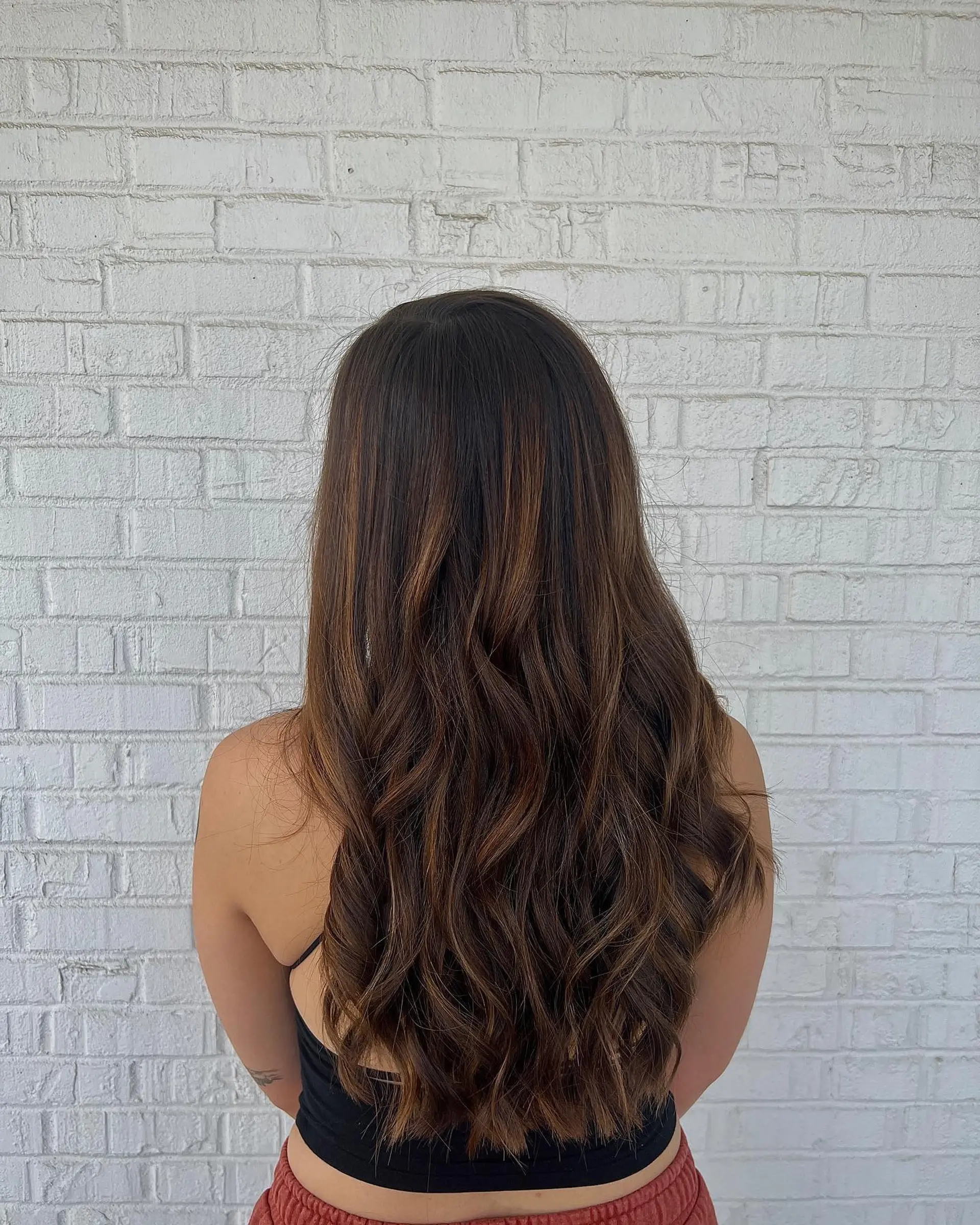 Long dark brown hair highlighted with warm caramel balayage and styled in relaxed, voluminous waves. 1