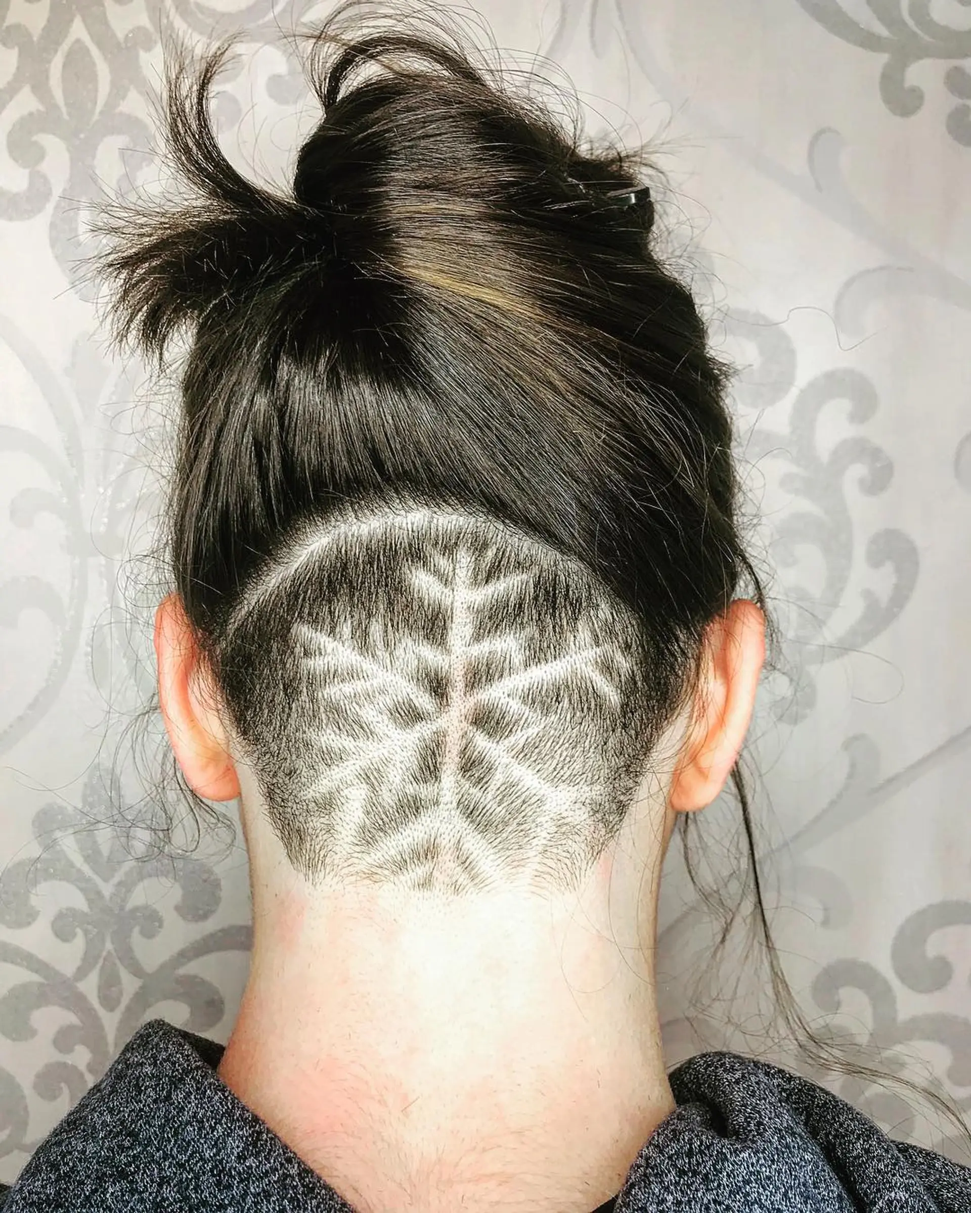A shaved nape undercut featuring an intricate etched snowflake hair tattoo design, with the longer upper hair secured in a top knot. 1