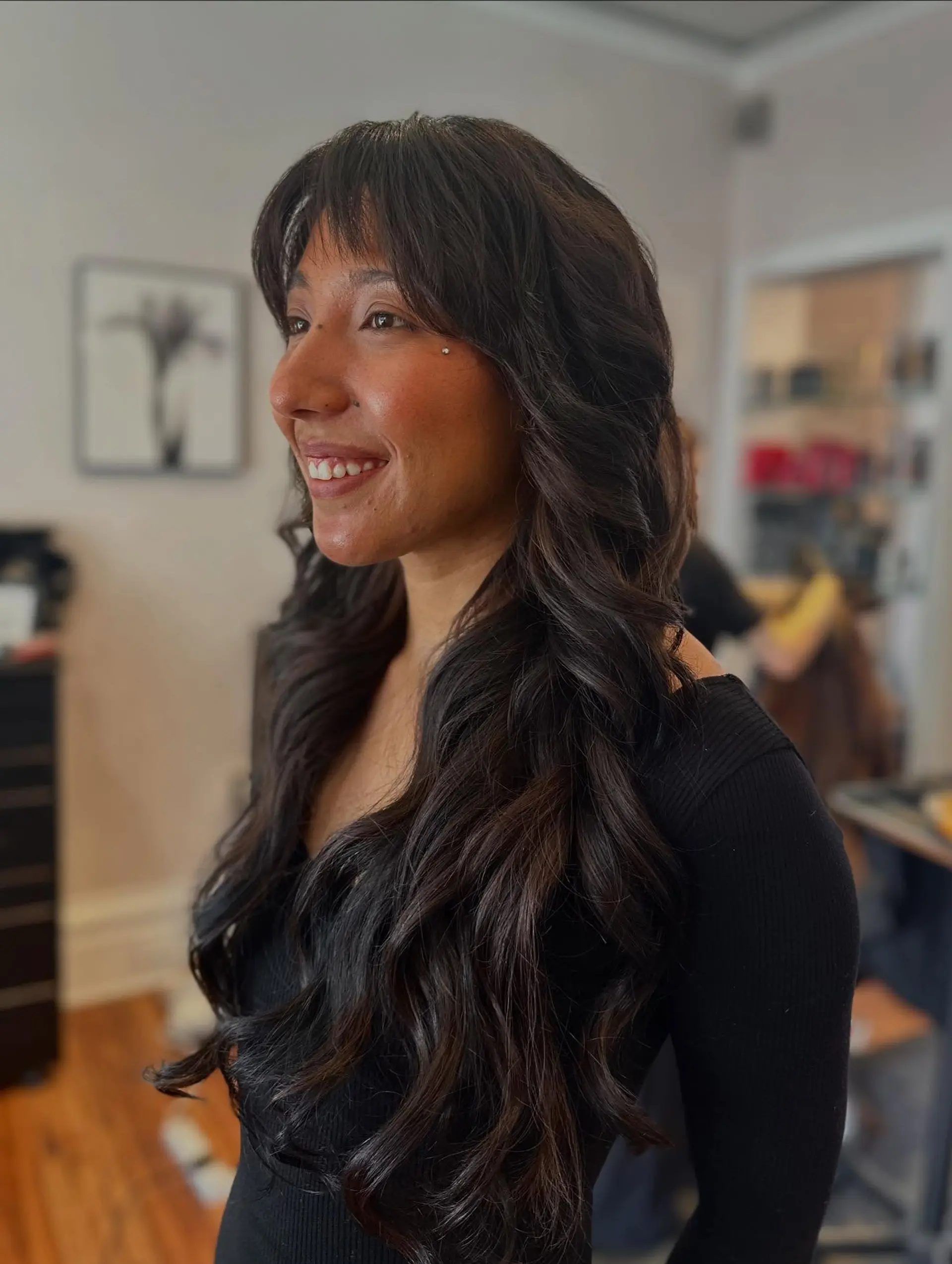 Long, dark brunette hair styled in loose, voluminous waves paired with textured bangs. 1