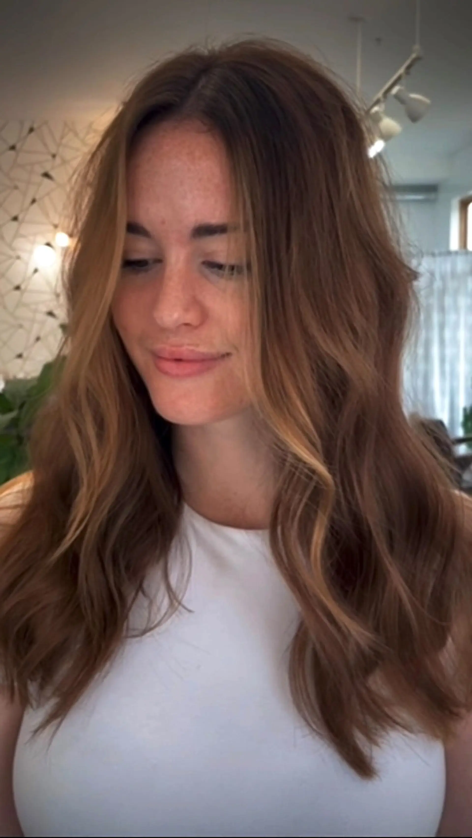 Long warm brunette hair styled in loose, soft waves with subtle face-framing lighter tones. 1