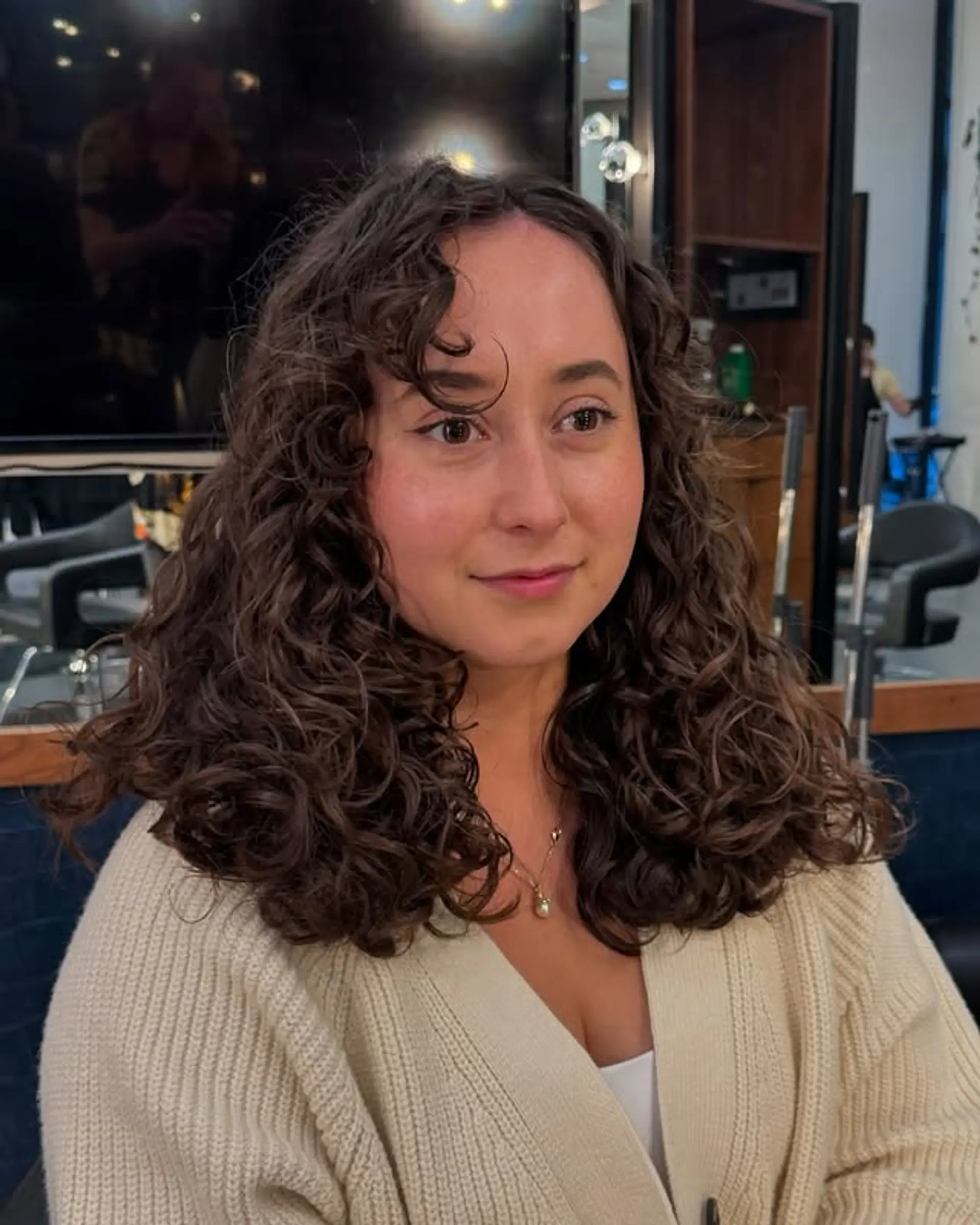A curly hairstyle with medium length, face-framing layers, and curly bangs. 1