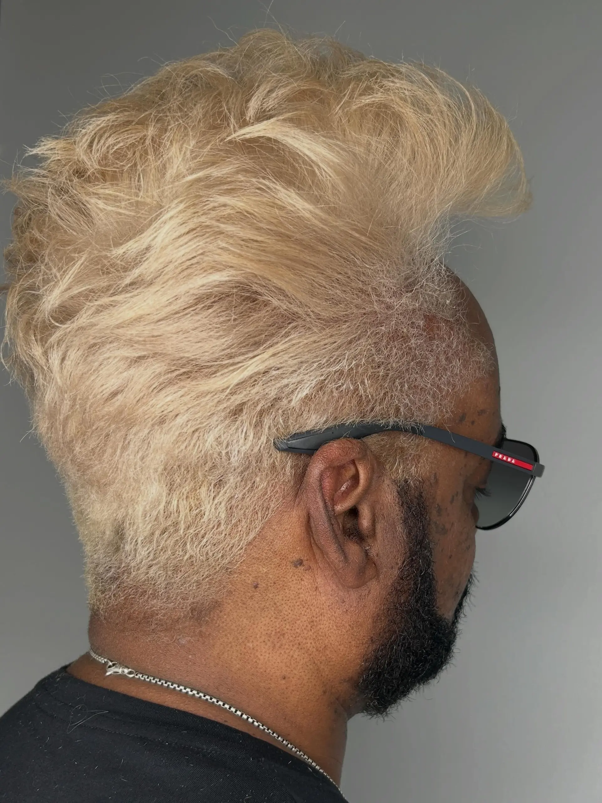 A high-volume, swept-back platinum blonde cut with tapered sides and a groomed dark beard for high contrast. 1