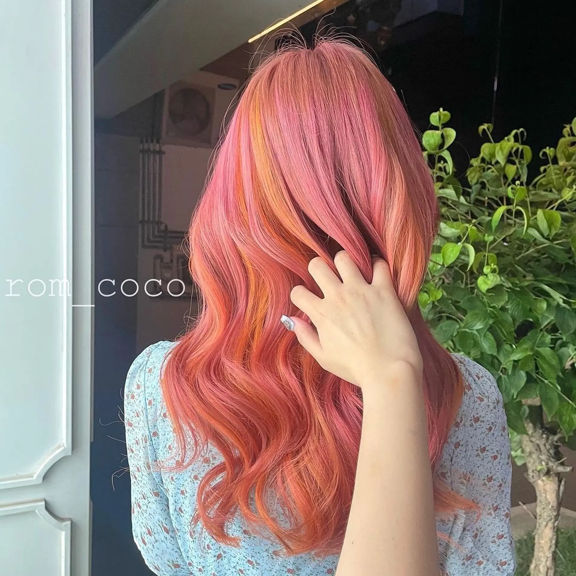 A wavy, long hairstyle with a balayage featuring pink and orange tones. 1