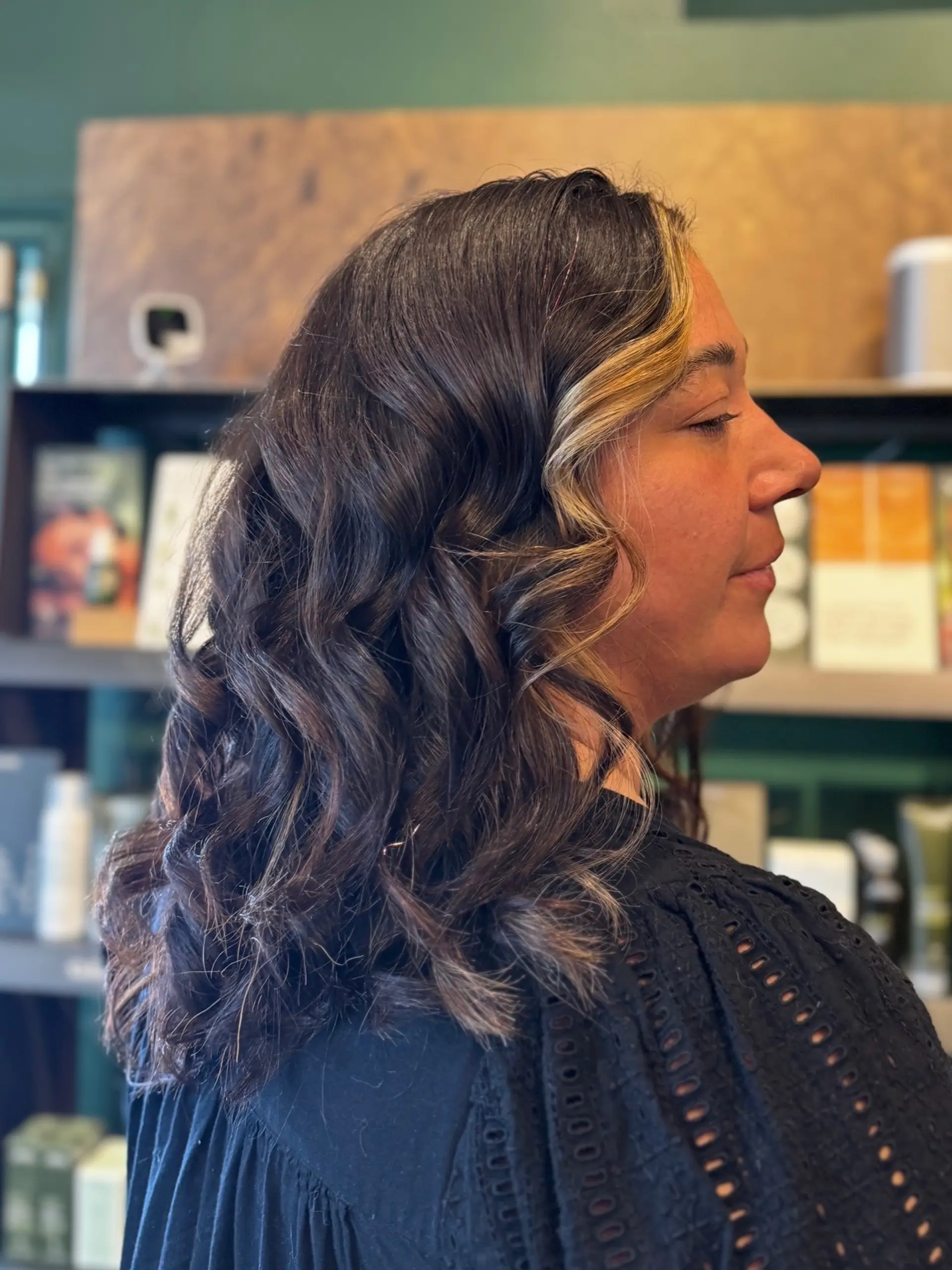 Medium-length dark brunette hair styled with soft loose waves and a bright face-framing money piece highlight. 1