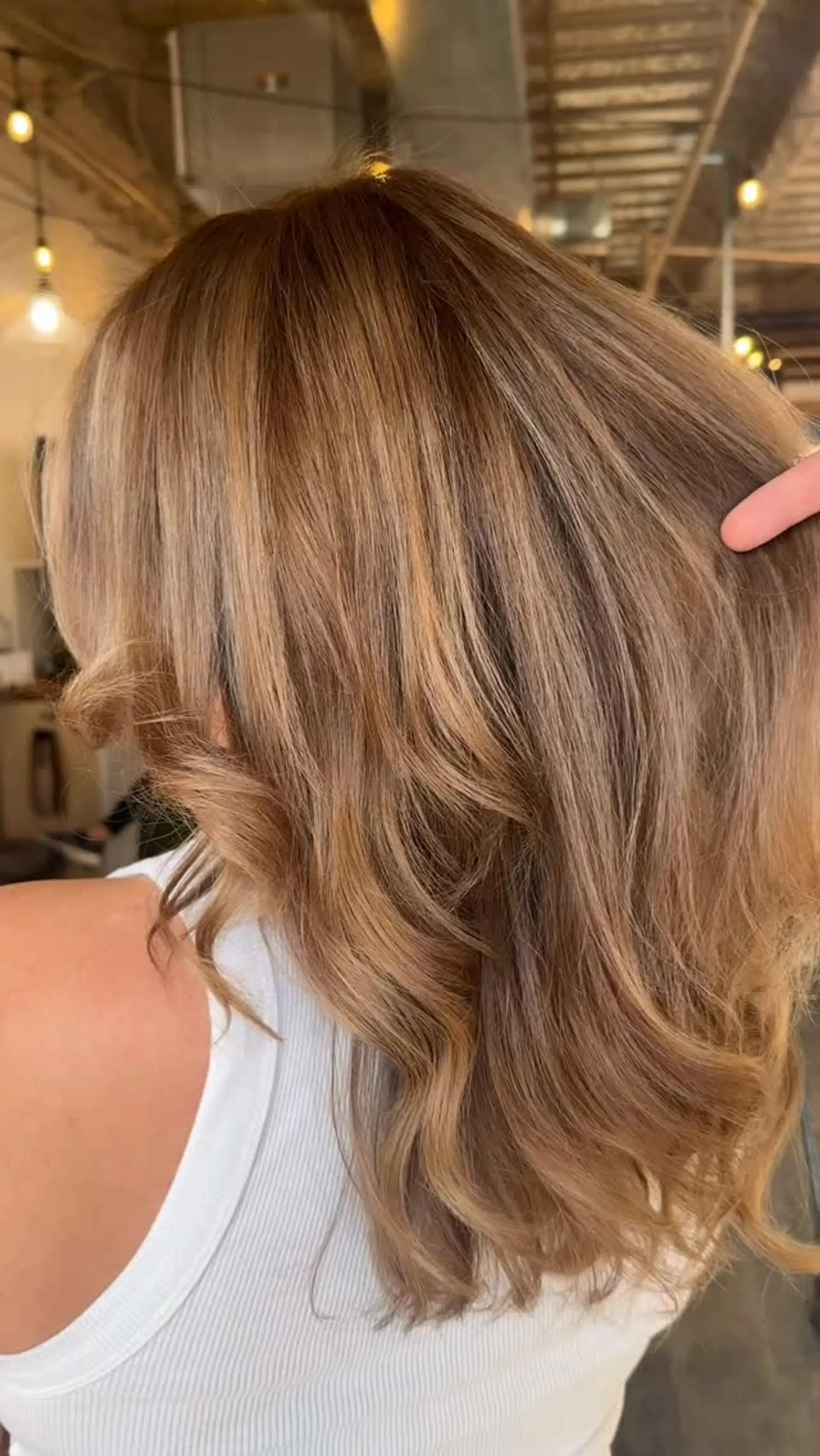 Shoulder-length dimensional warm light brown and honey blonde hair styled with a smooth, soft-waved blowout. 1