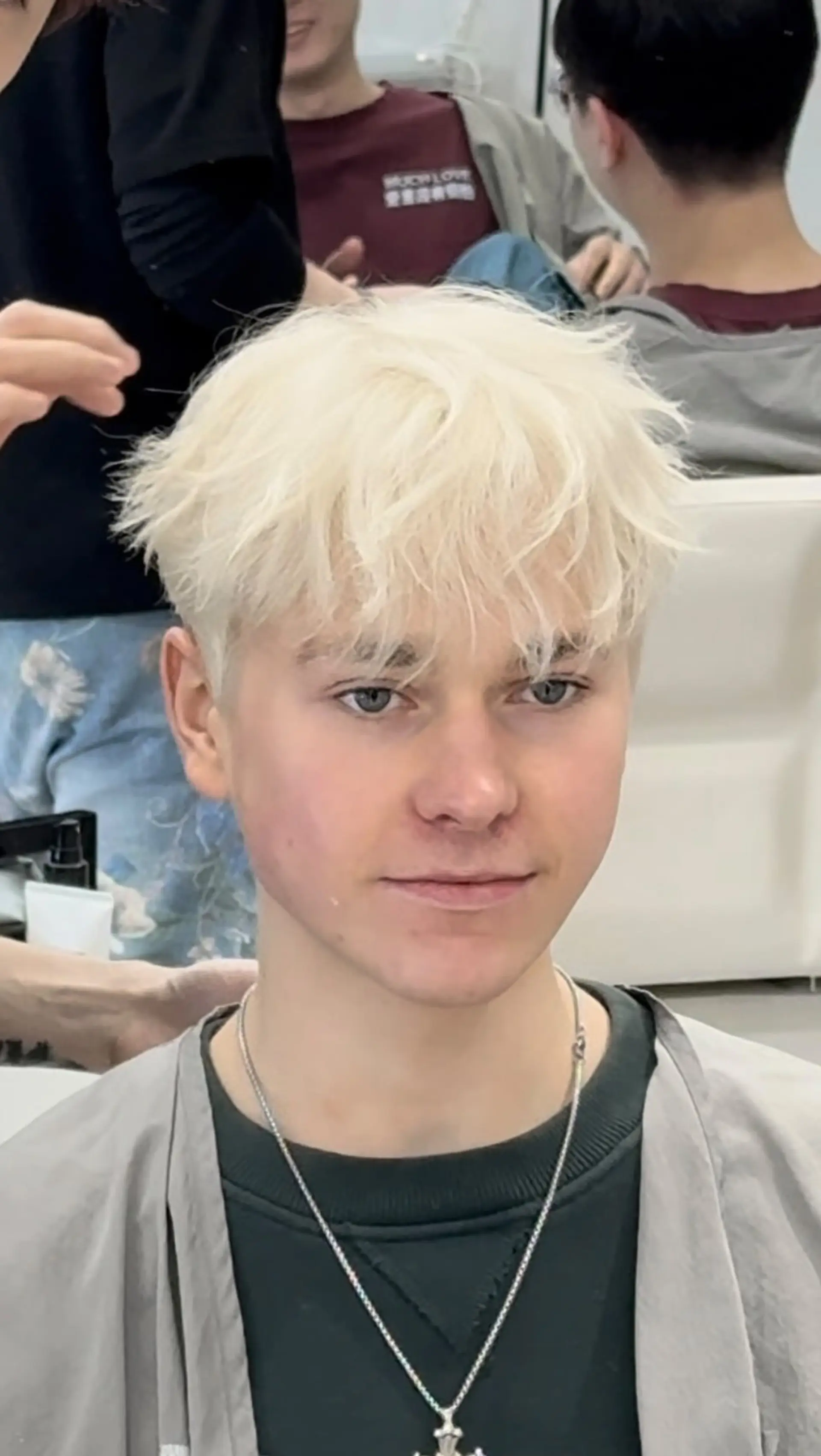 A textured short crop in an ultra-light platinum blonde shade, styled with piecey, tousled bangs falling over the forehead. 1