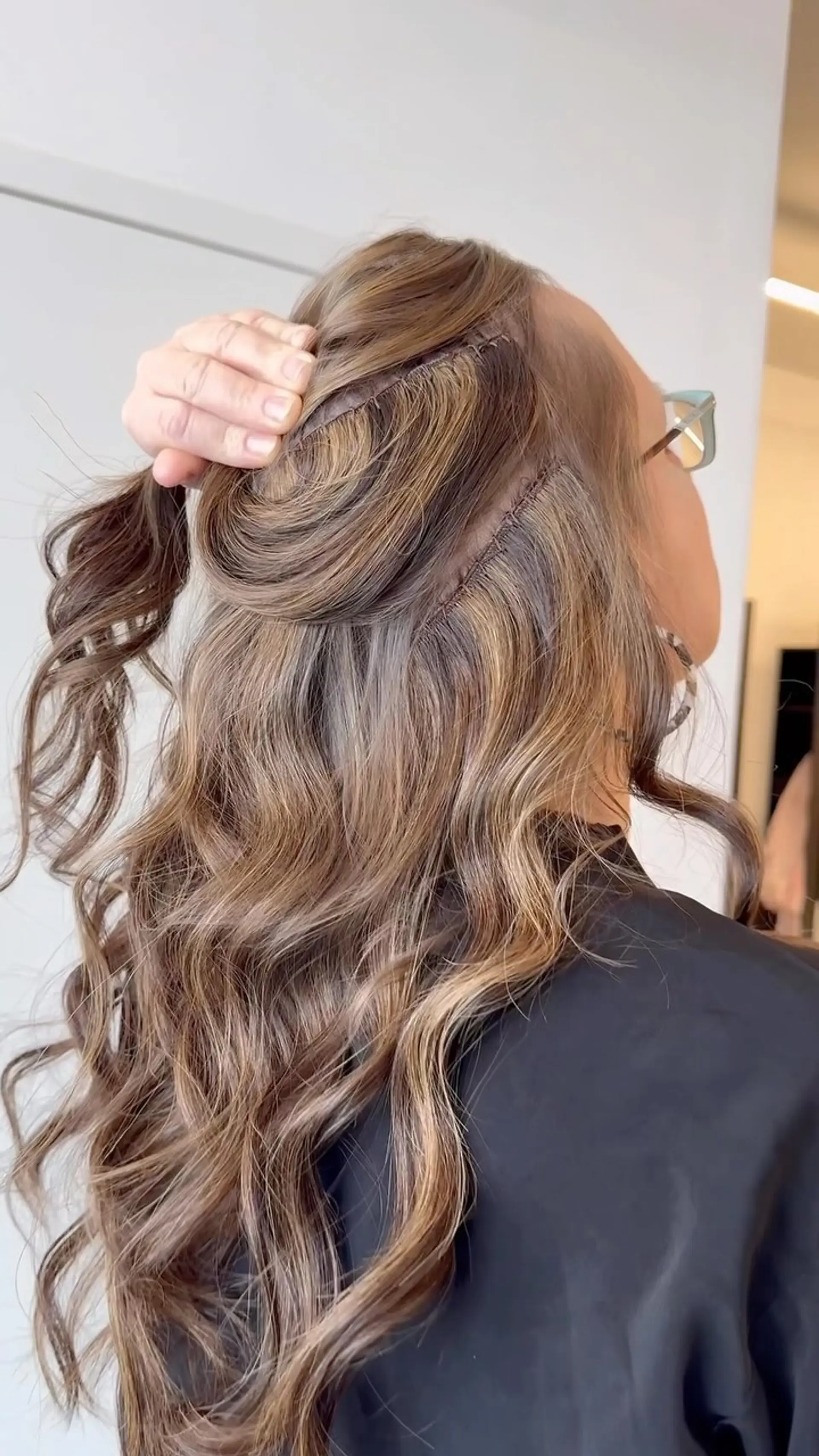 Sew-in weft hair extensions displayed on long, loose wavy hair with dimensional caramel and light brown tones. 1