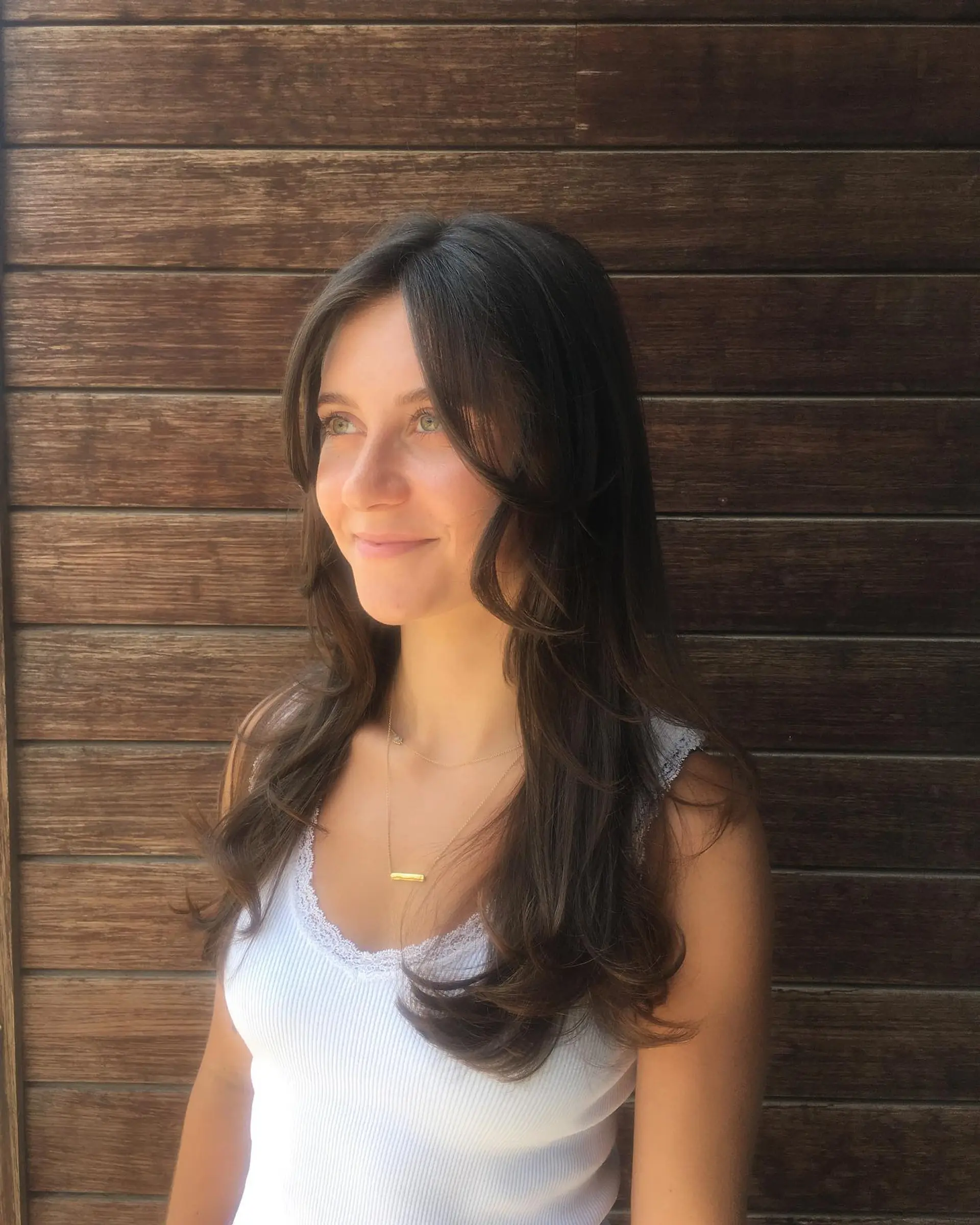Long dark brown hair cut with soft face-framing curtain bangs and loose layered curls at the ends. 1