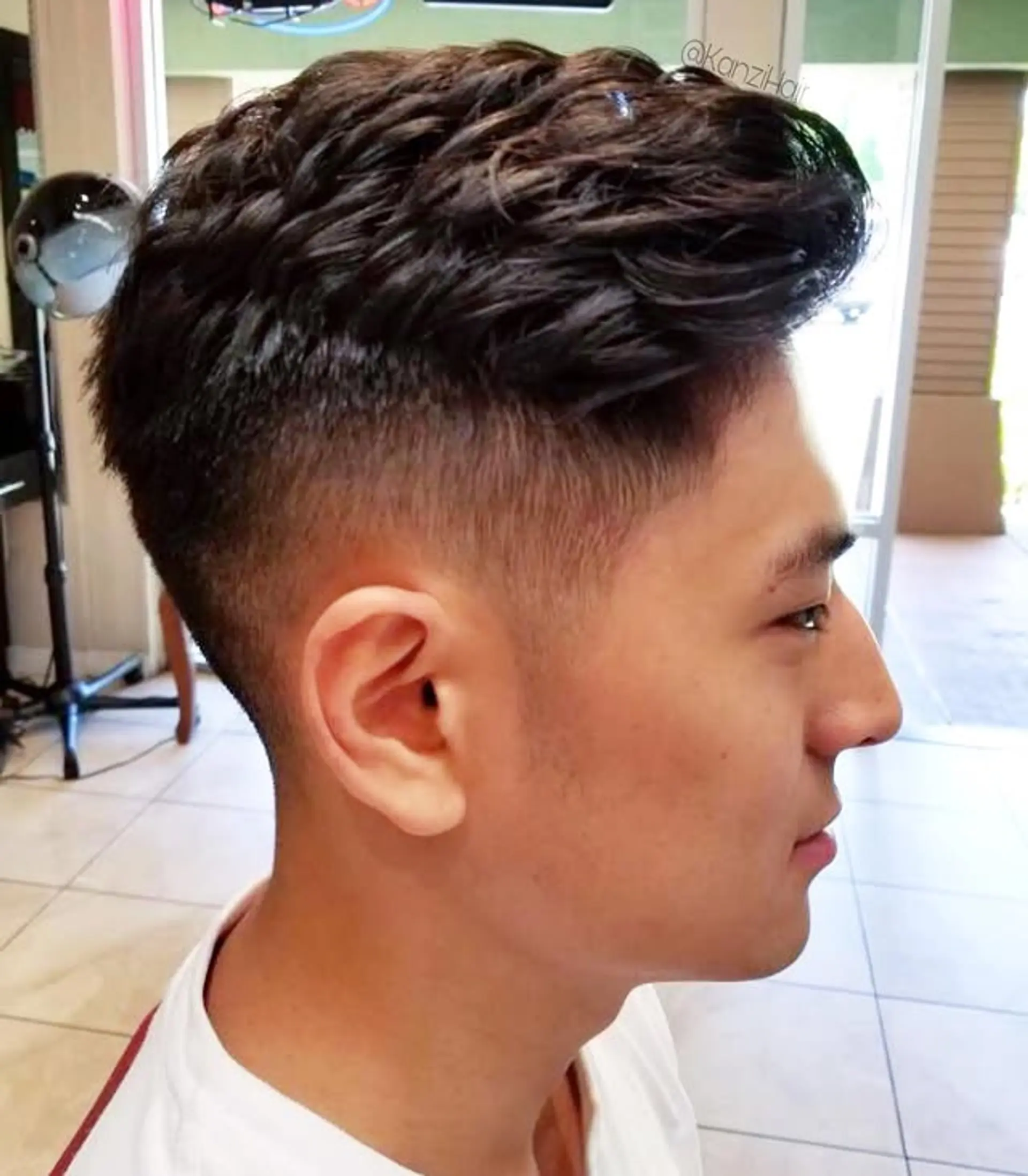 A contemporary men's haircut showcasing a high fade on the sides and back, paired with a voluminous, textured, and wavy top. 1