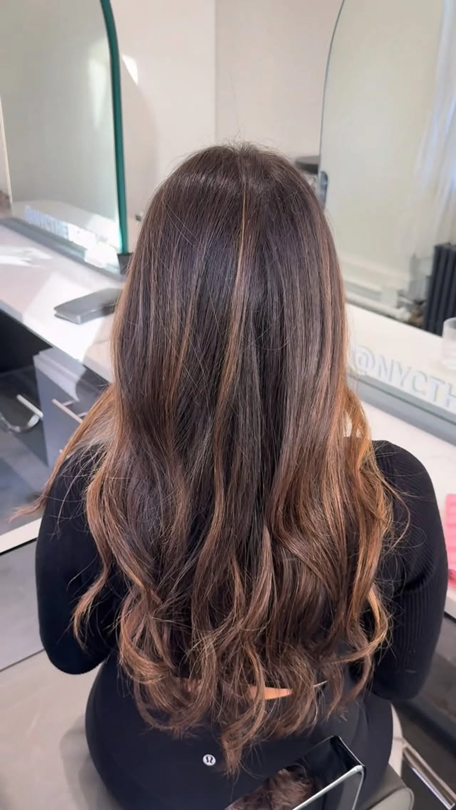 Long dark brown hair enhanced with subtle caramel balayage ribbons and styled in loose, soft waves. 1