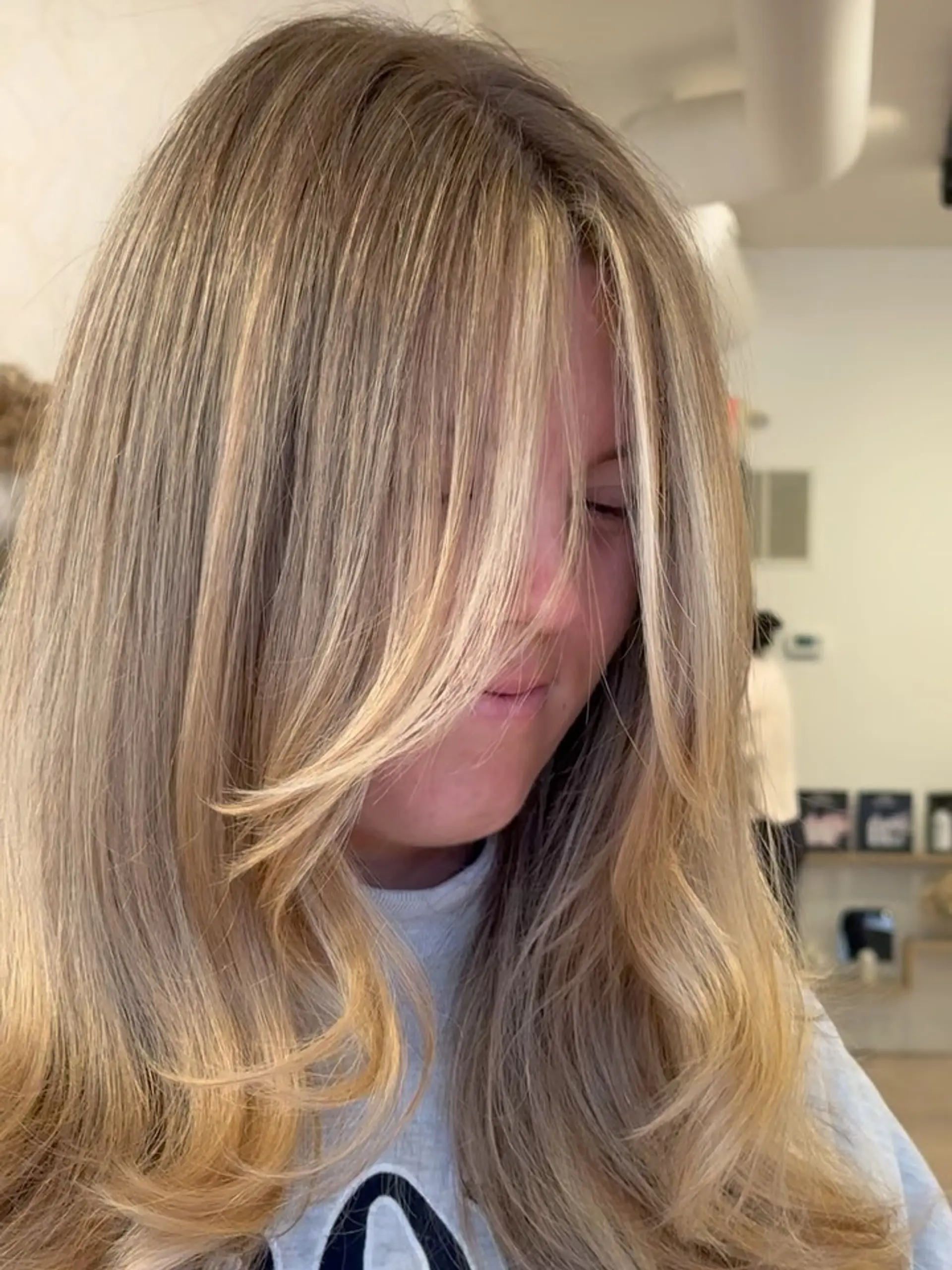 Dimensional honey blonde hair cut with face-framing curtain bangs and styled in a soft blowout. 1