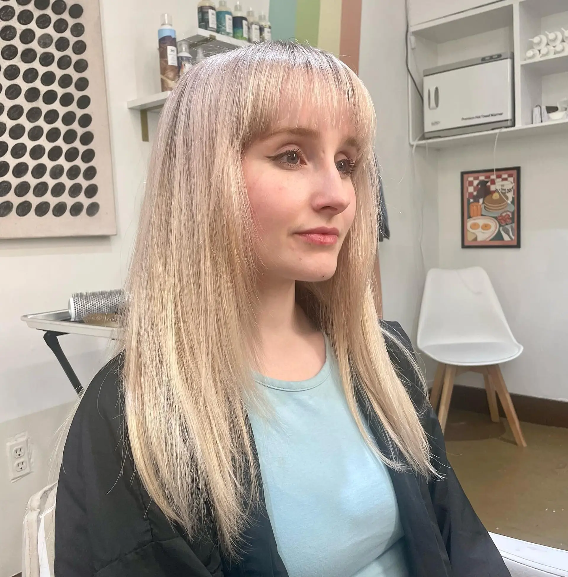 A medium-length shag haircut with face-framing layers and Bardot bangs. The hair is a cool-toned, icy platinum blonde. 1