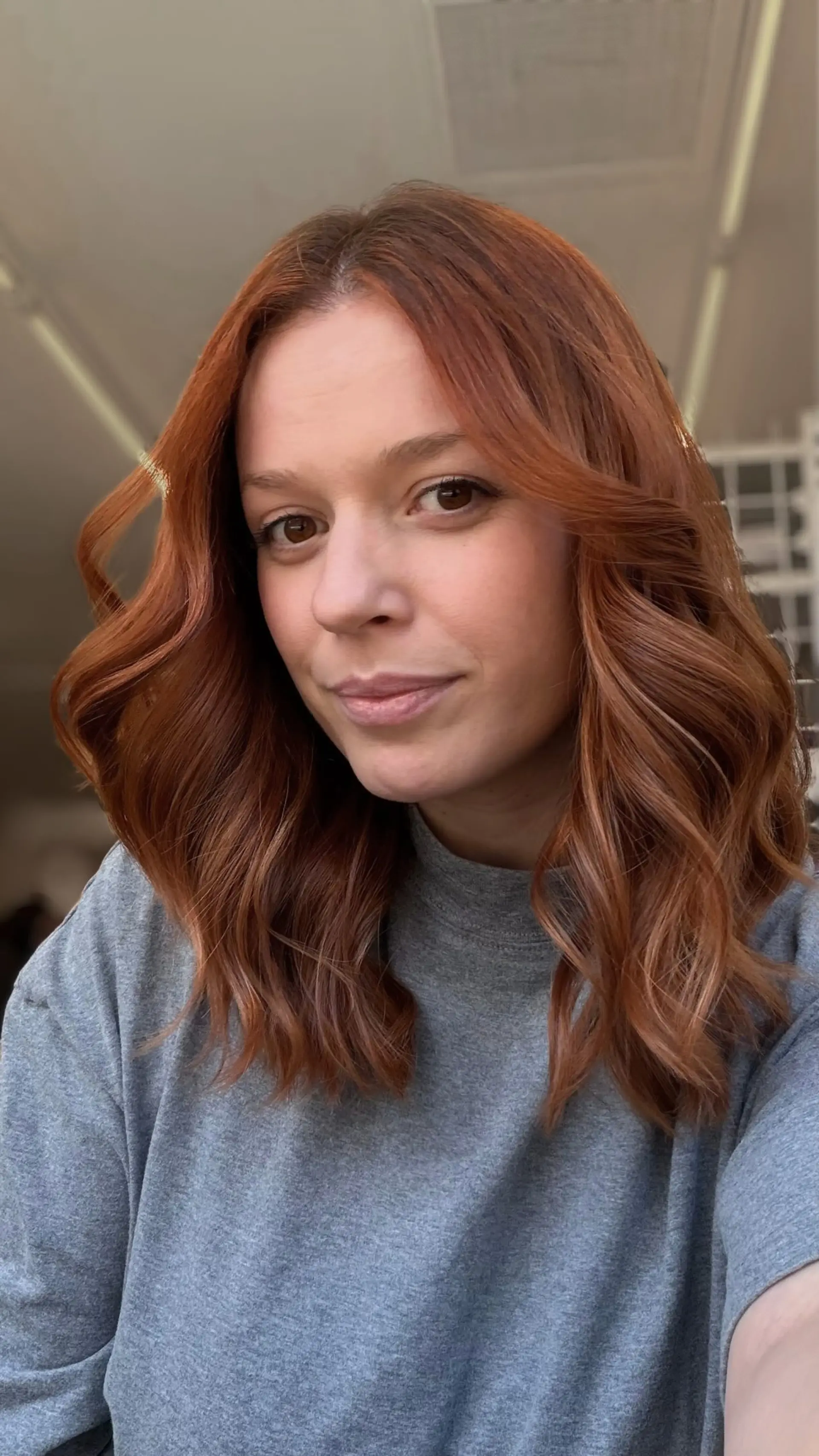 Medium-length auburn hair with subtle dimensional brightness, styled in soft loose waves with a center part. 1