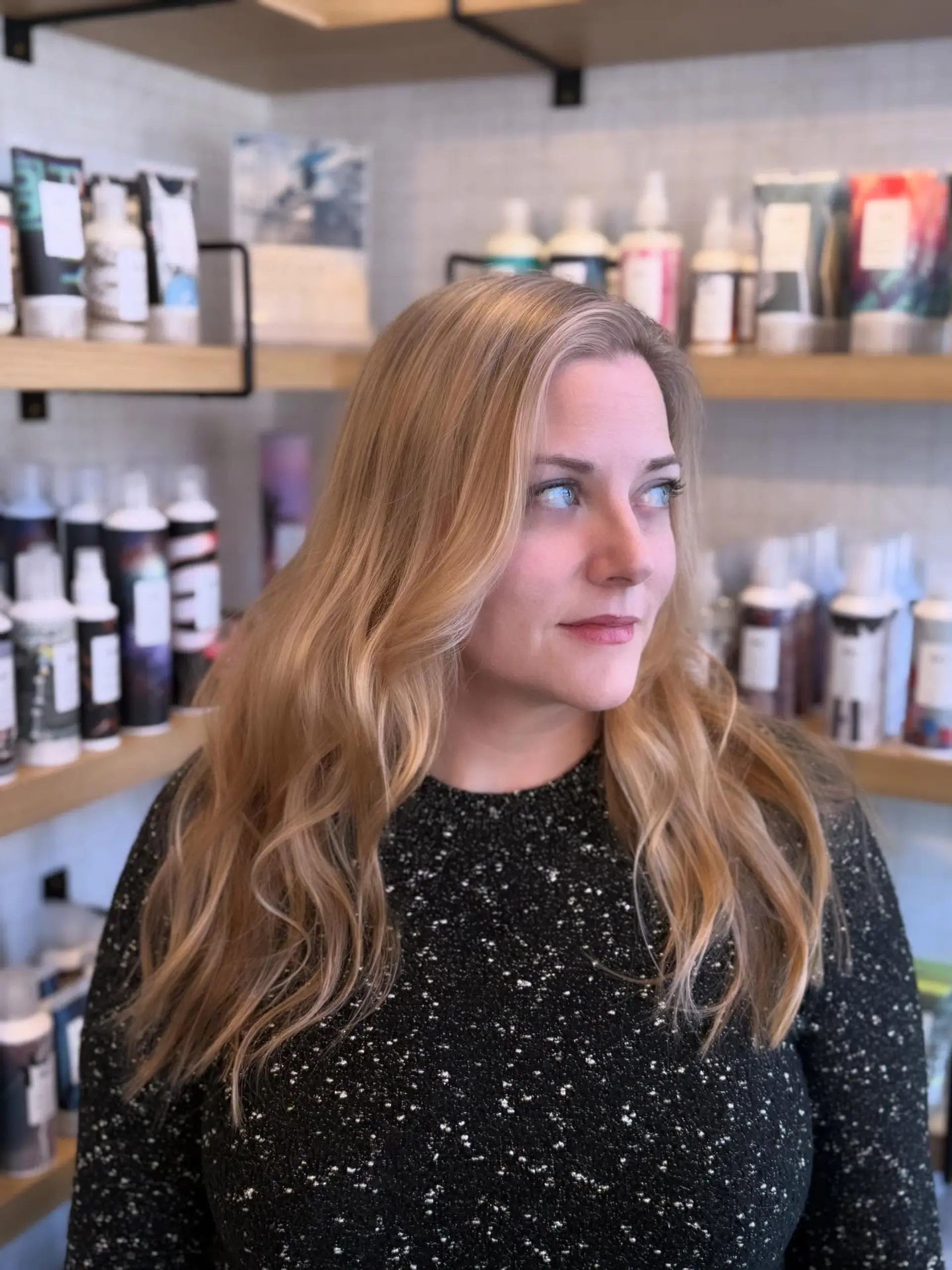 Long warm golden blonde hair styled in soft, loose waves with a deep side part. 1