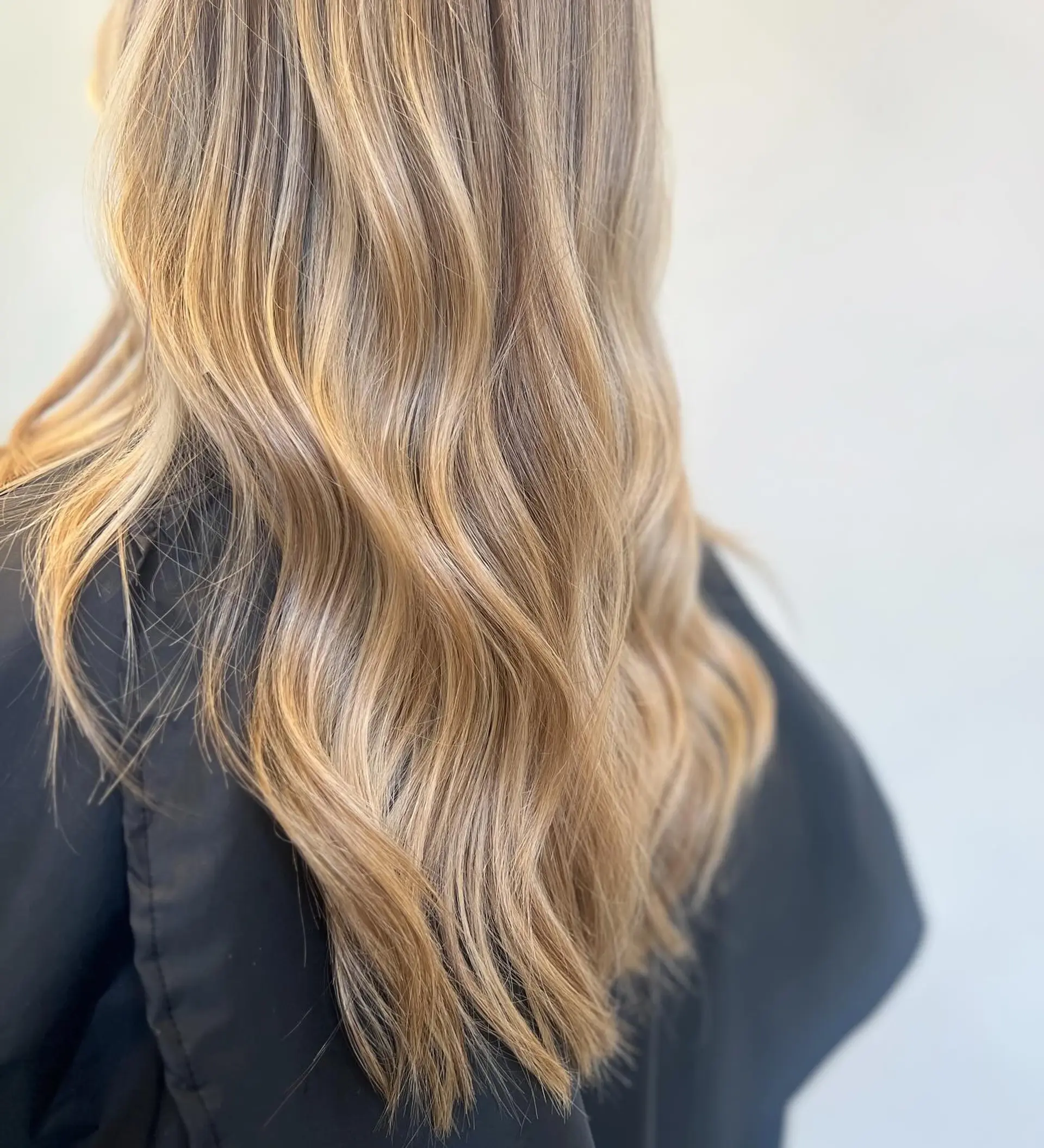 Long warm golden blonde hair styled in soft, cascading loose waves. 1