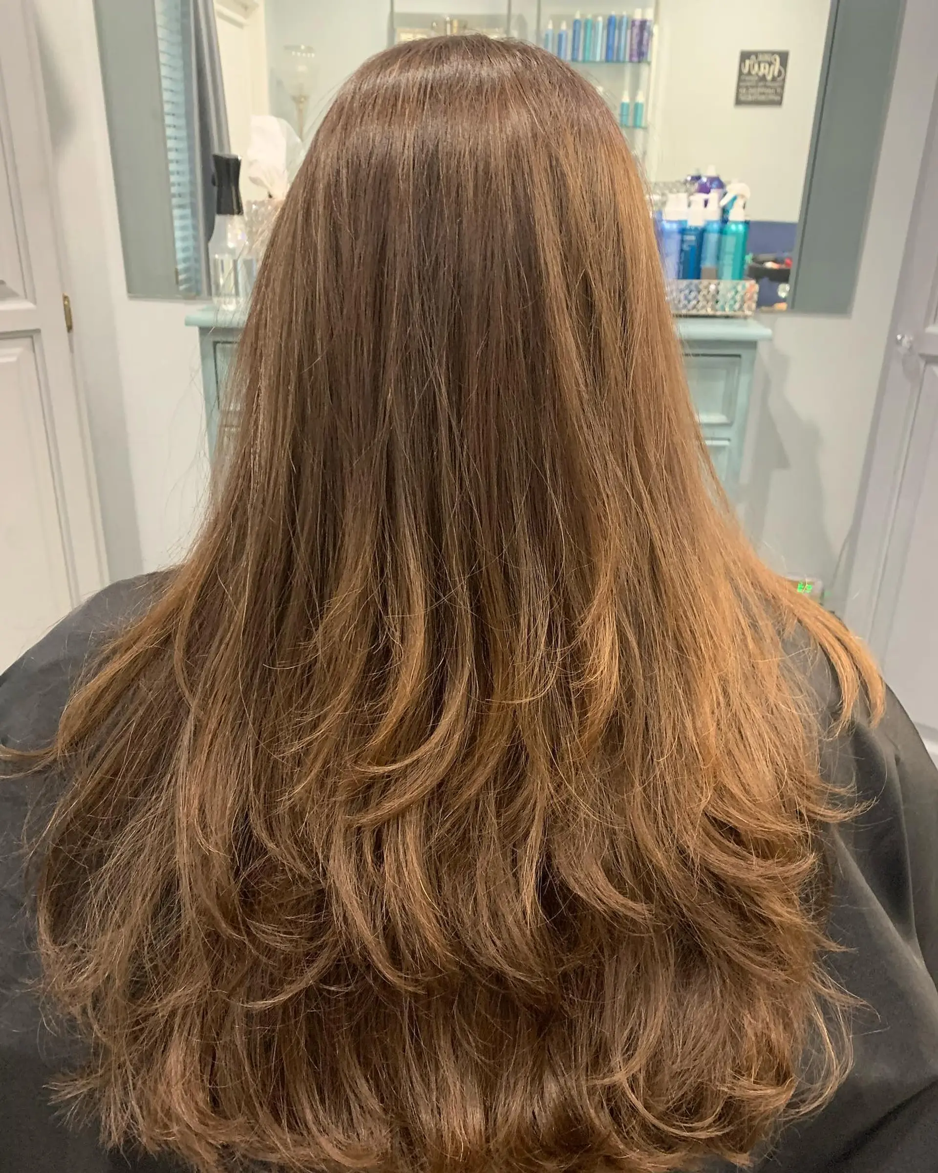 Long warm brunette hair styled with cascading feathered layers and softly flipped ends. 1