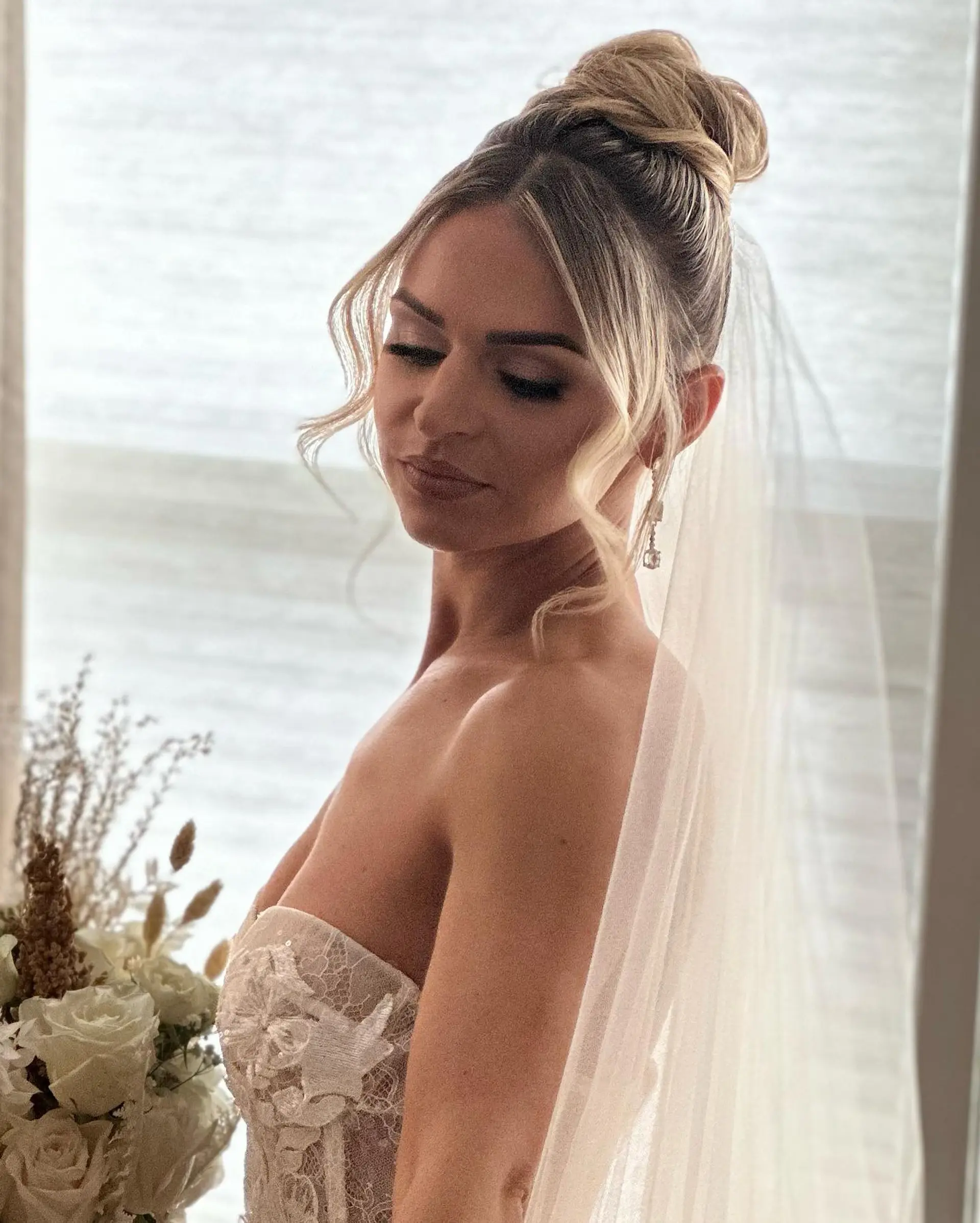A sophisticated bridal high bun with soft, wavy face-framing pieces and a bridal veil. 1