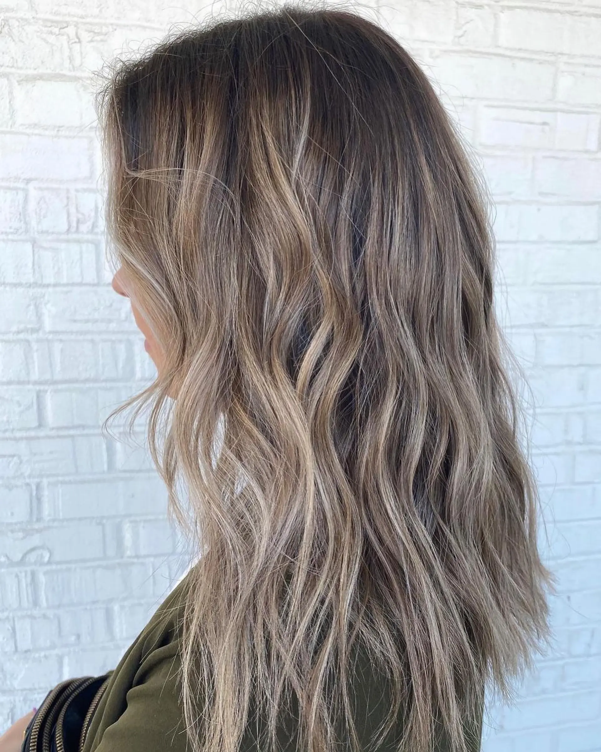 A dimensional bronde balayage seamlessly blended from a dark base into sun-kissed blonde tones, styled with relaxed, textured waves. 1