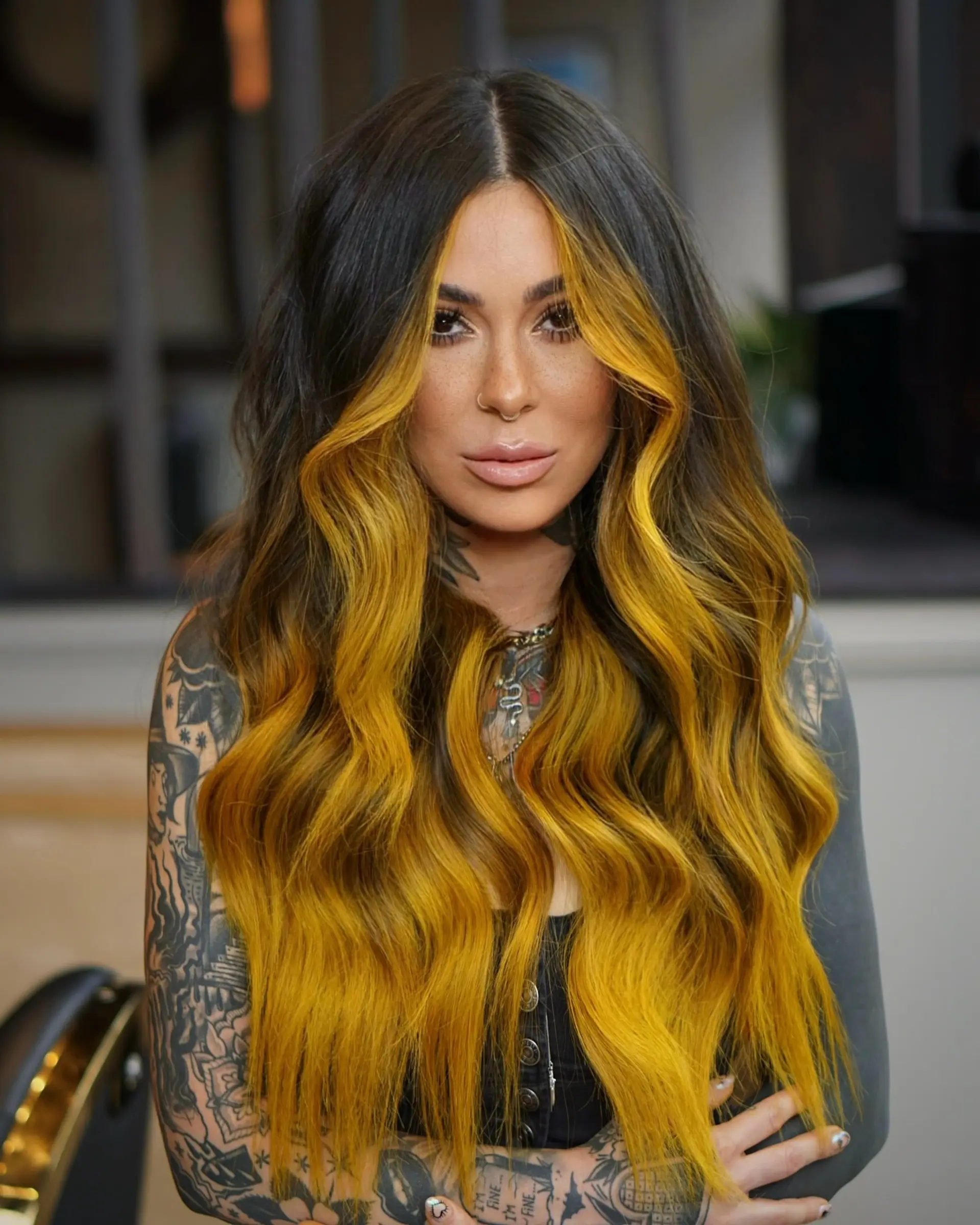 Long wavy dark hair featuring a bold golden-yellow face-framing money piece and warm balayage highlights. 1