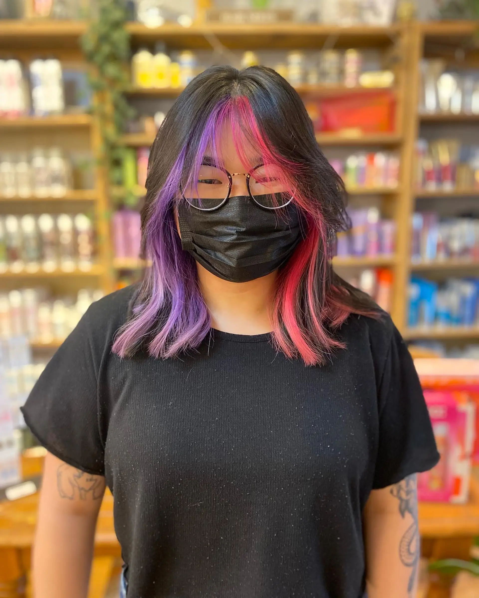 This medium length hairstyle features bold, chunky highlights in pink and purple, creating a striking contrast against the black base.  1