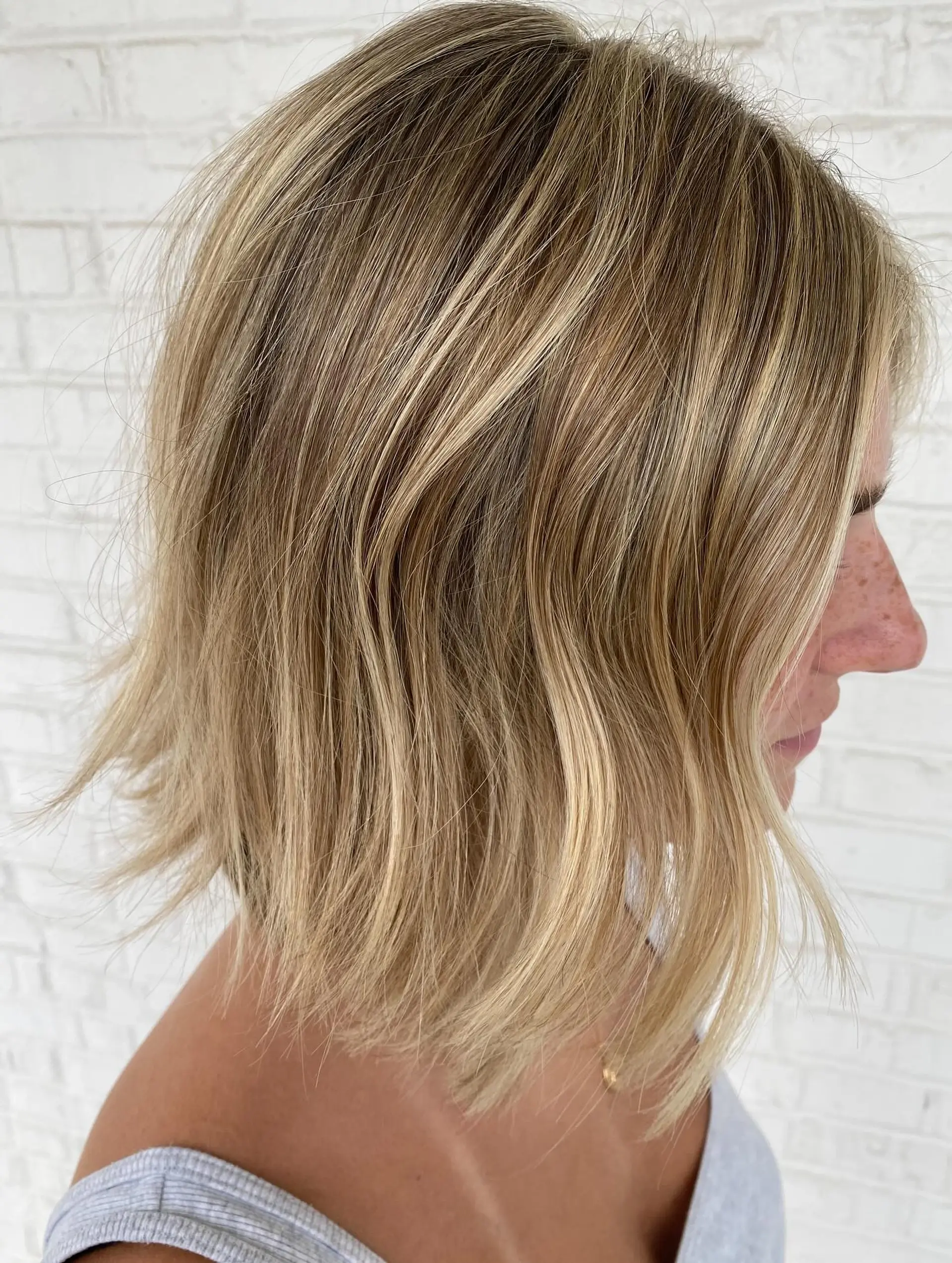 A textured, collar-skimming bob featuring multi-dimensional blonde highlights and soft, subtle waves. 1