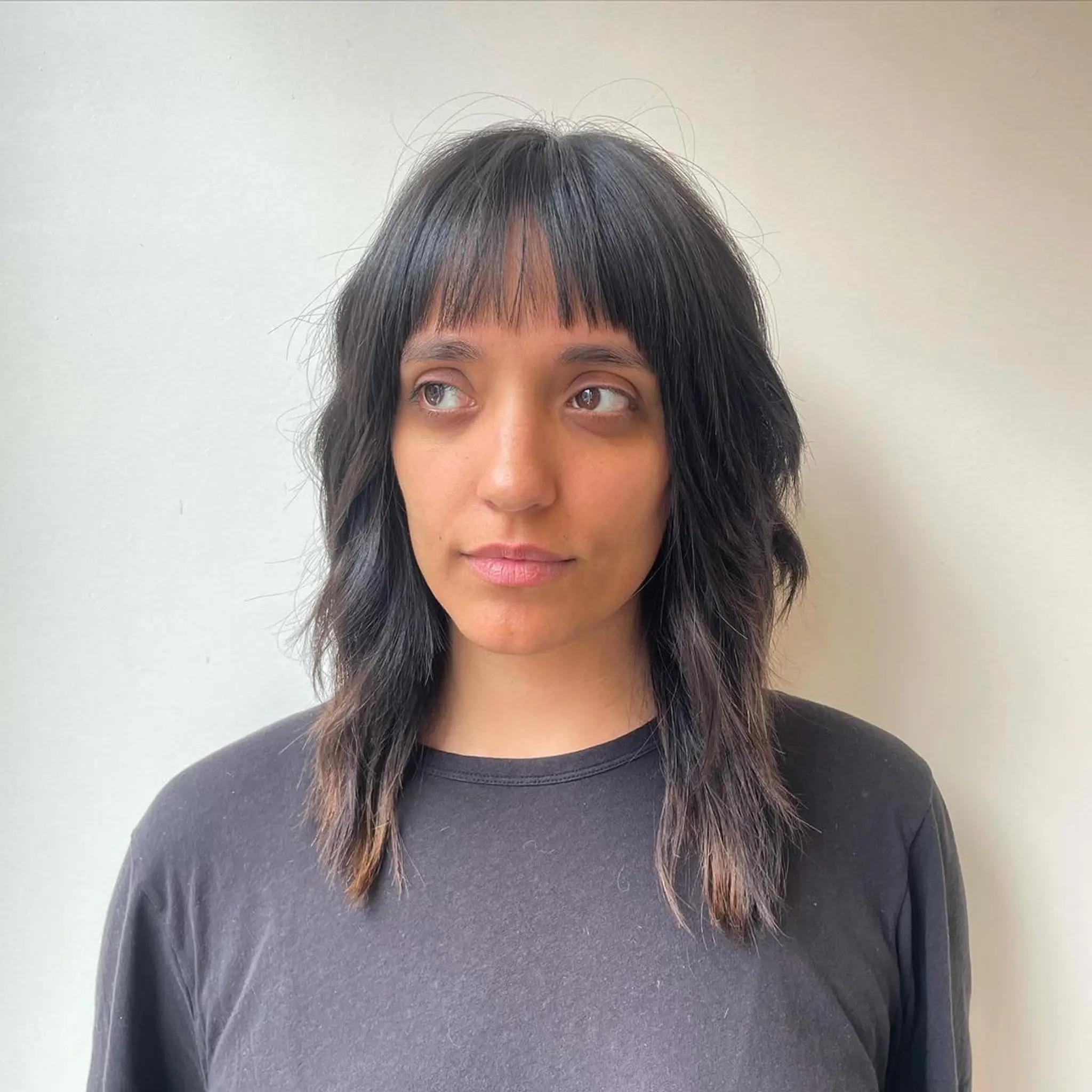 Medium-length wavy cut with a soft fringe and dark brown hair featuring light brown highlights, offering a layered texture.