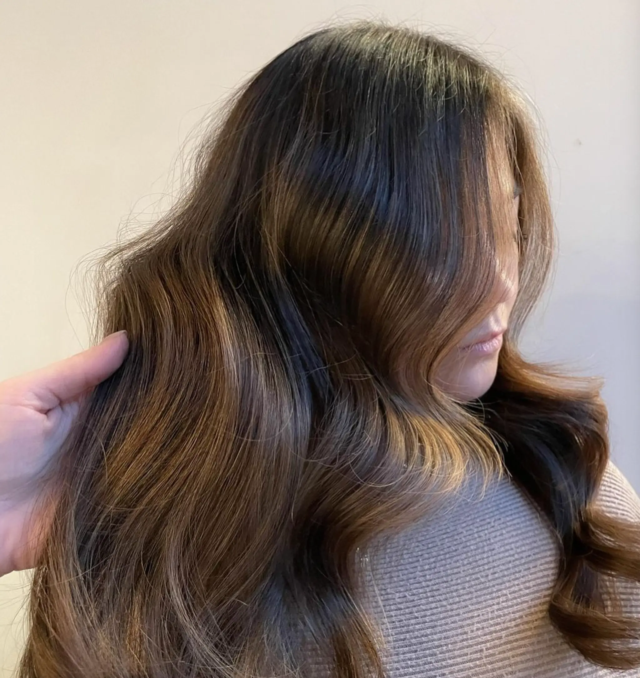 An intricate long wavy hairstyle with dark brown base color, accentuated by lighter brown and honey blonde balayage highlights. 