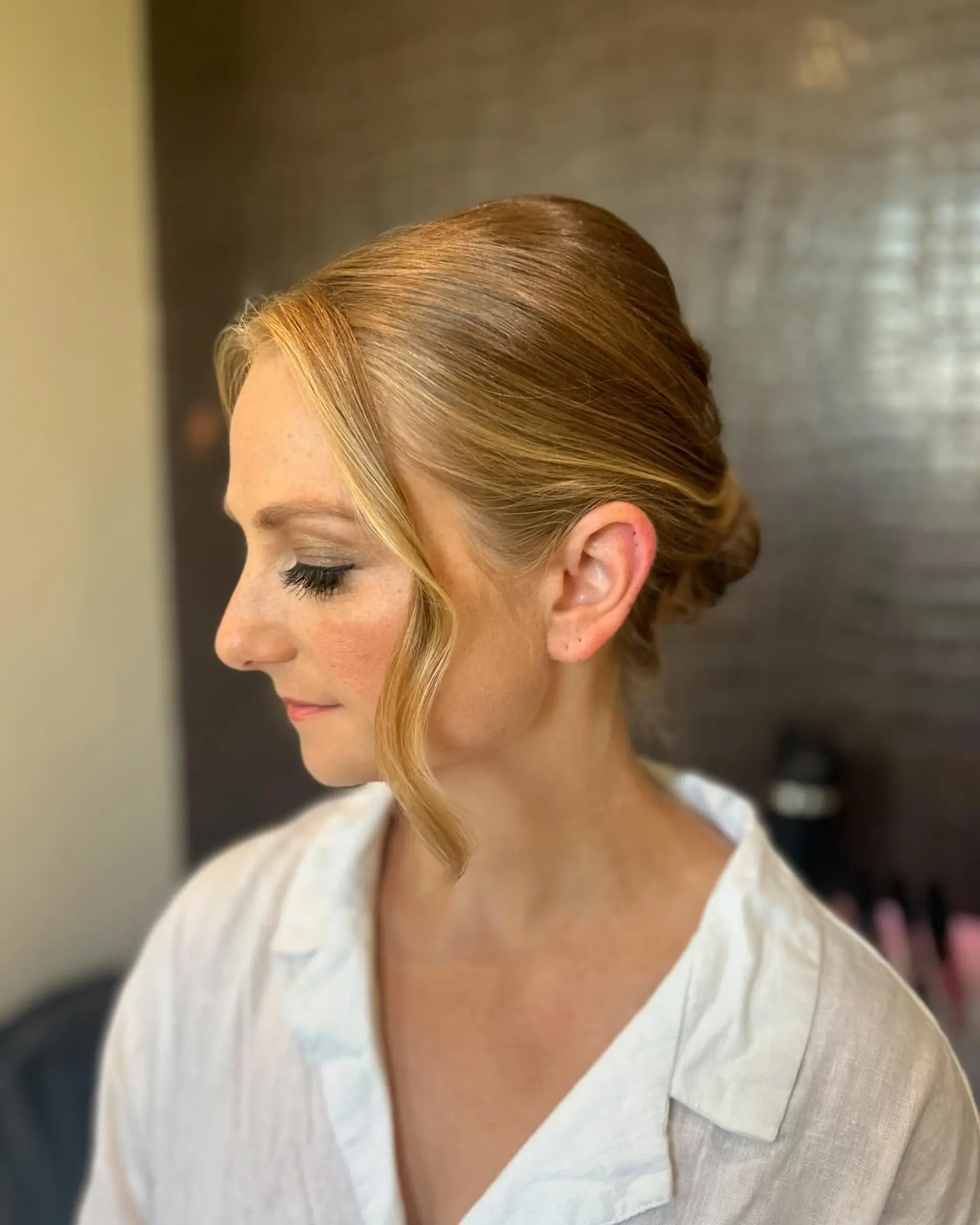 An elegant bridal updo smoothly gathered at the back with a softly curled face-framing tendril. 1