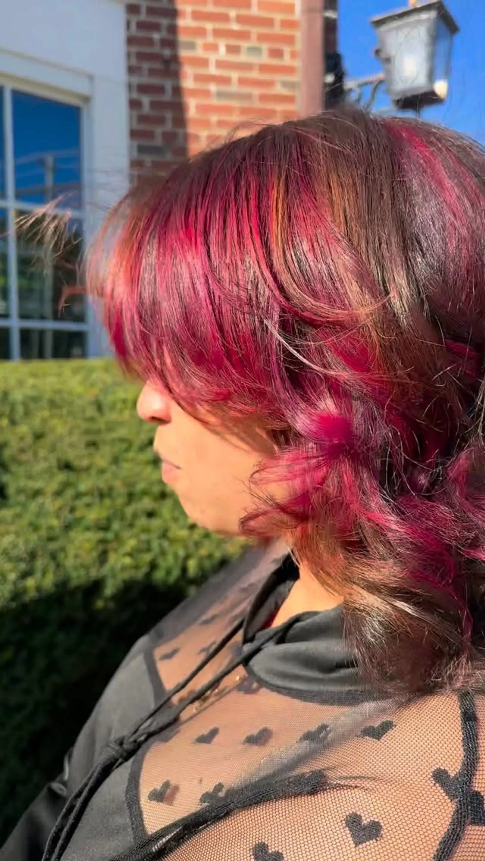Shoulder-length dark brown hair accented with vivid magenta and burgundy highlights, styled with full textured bangs and loose wavy ends. 1