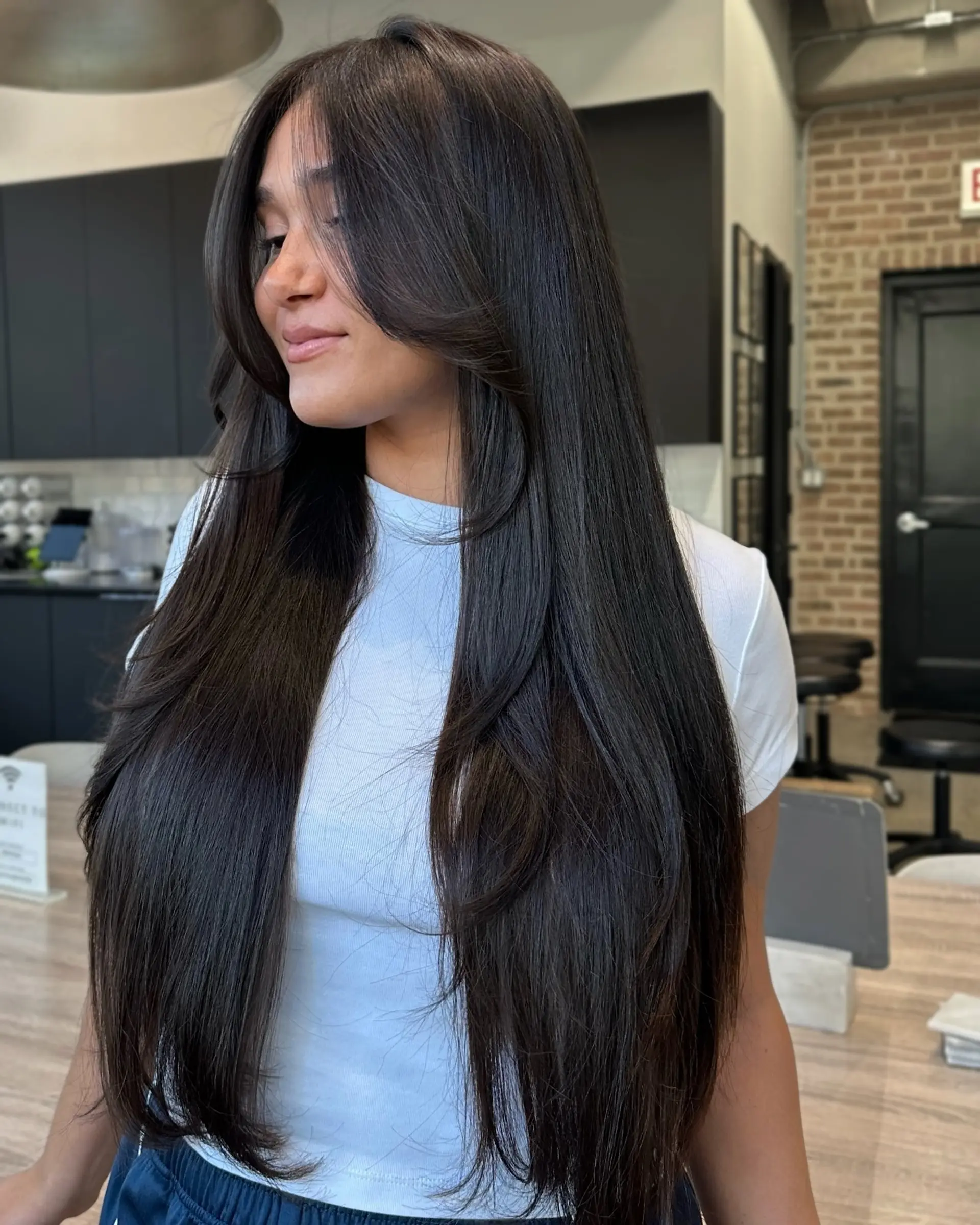 A long layered haircut with center-parted curtain bangs. 1