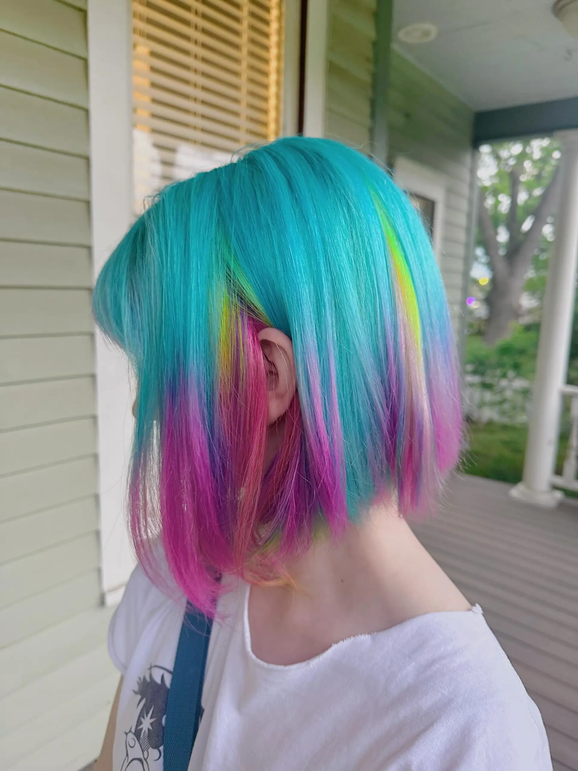A short, blunt bob styled with a vibrant turquoise and teal main color, accented by hidden peek-a-boo panels of hot pink, purple, and yellow-green, creating a striking multi-dimensional effect. 1
