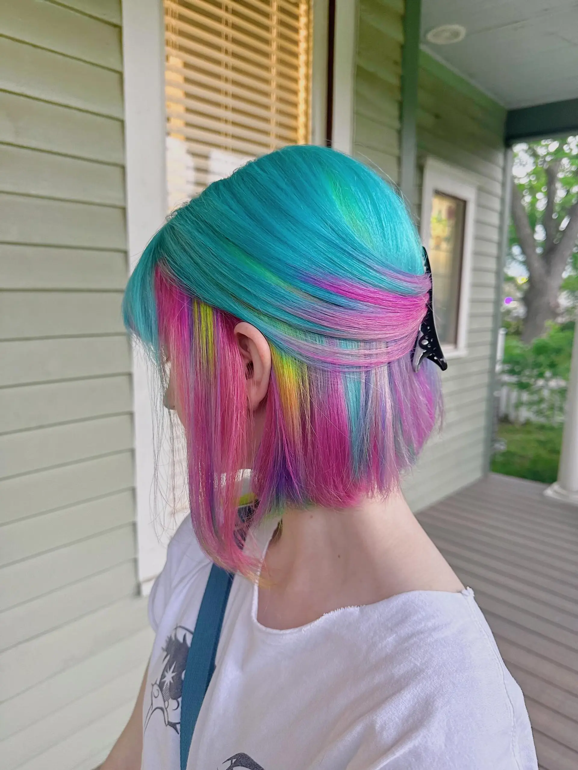 A short, blunt bob styled with a vibrant turquoise and teal main color, accented by hidden peek-a-boo panels of hot pink, purple, and yellow-green, creating a striking multi-dimensional effect. 2