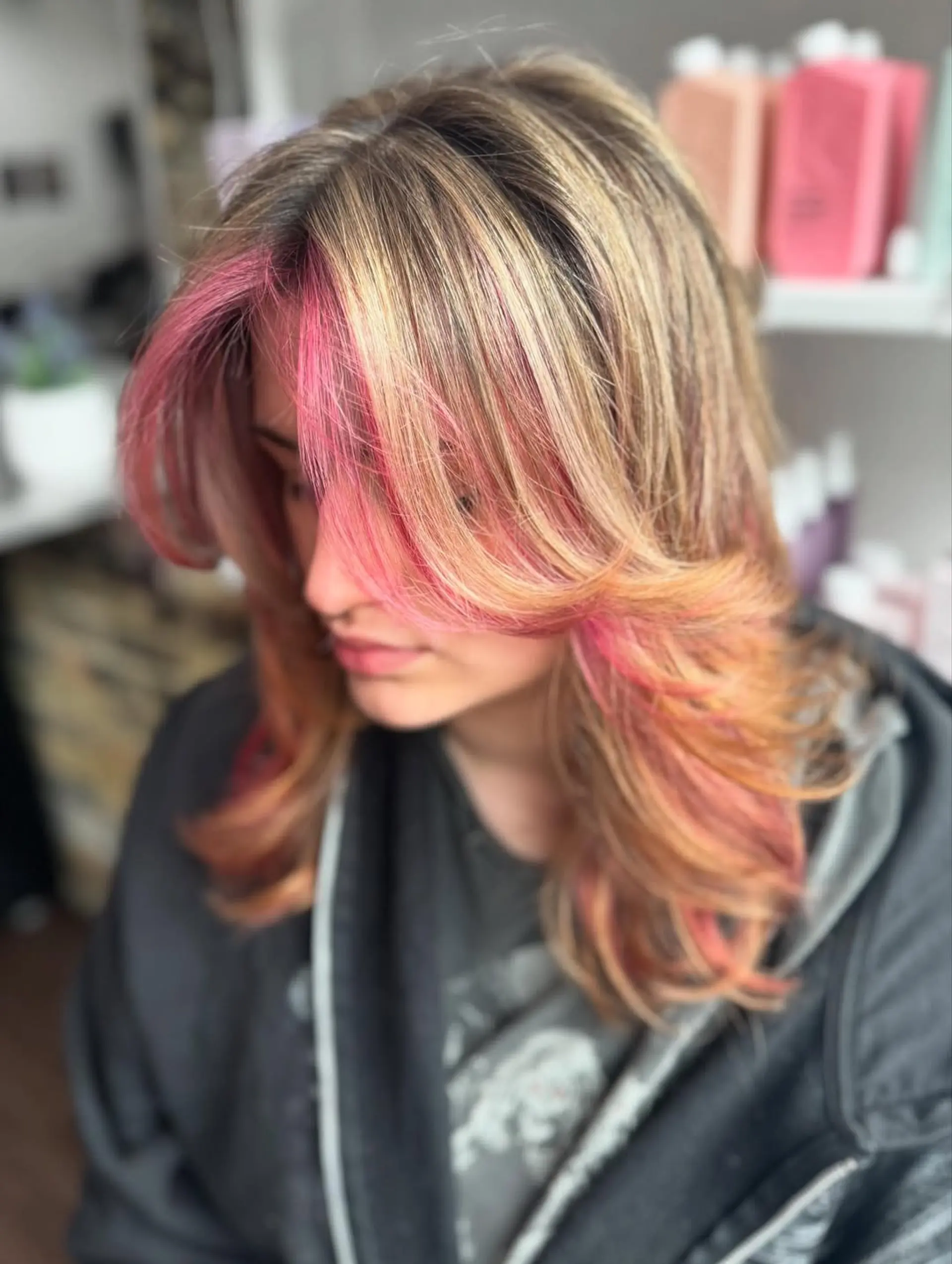 A stylish medium-length haircut featuring voluminous butterfly layers and bold face-framing money piece highlights in vibrant hot pink and peach tones on a dimensional light brown/dirty blonde base. 1