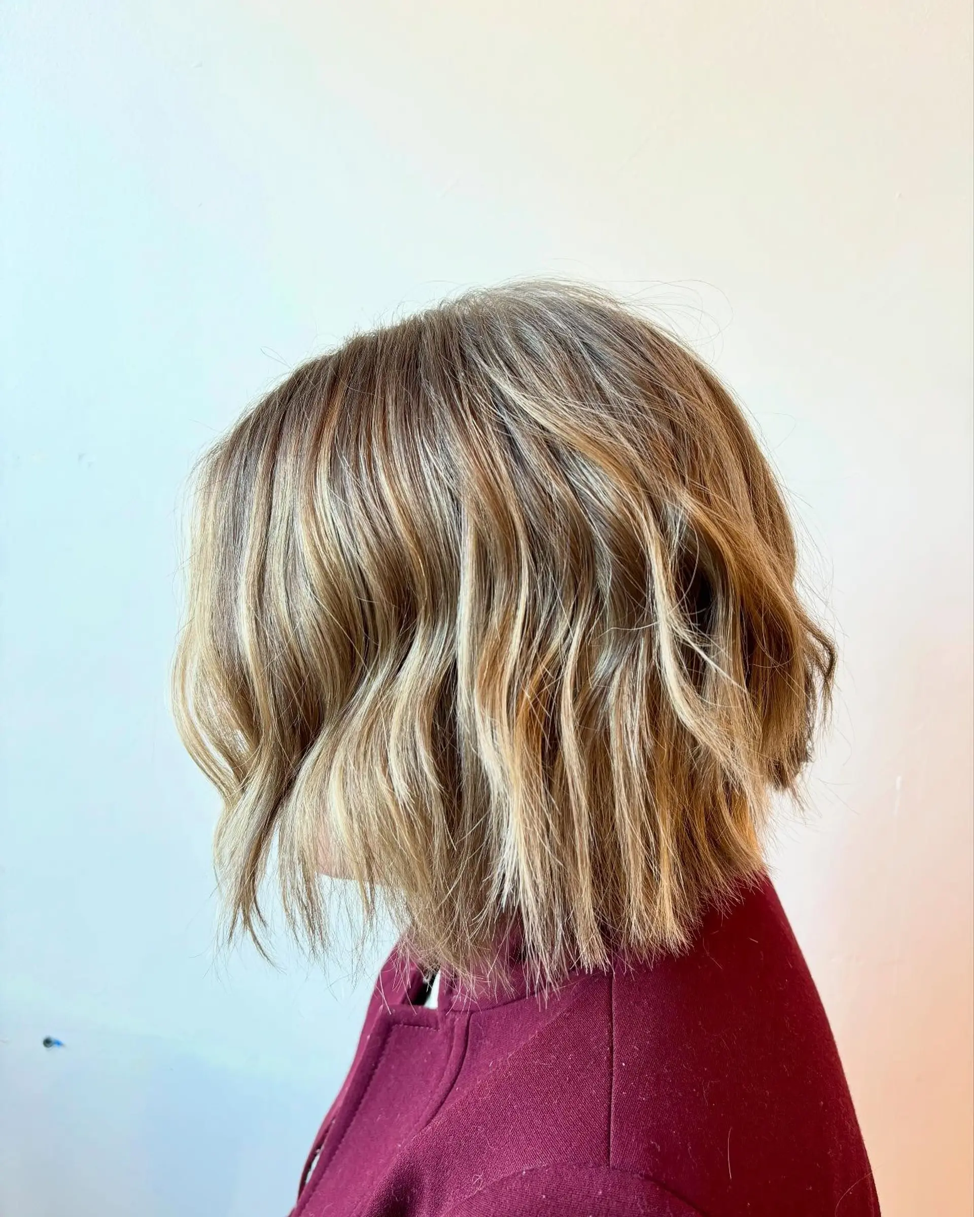 A choppy, chin-length textured bob enhanced with dimensional blonde balayage highlights and styled with loose, relaxed waves. 1