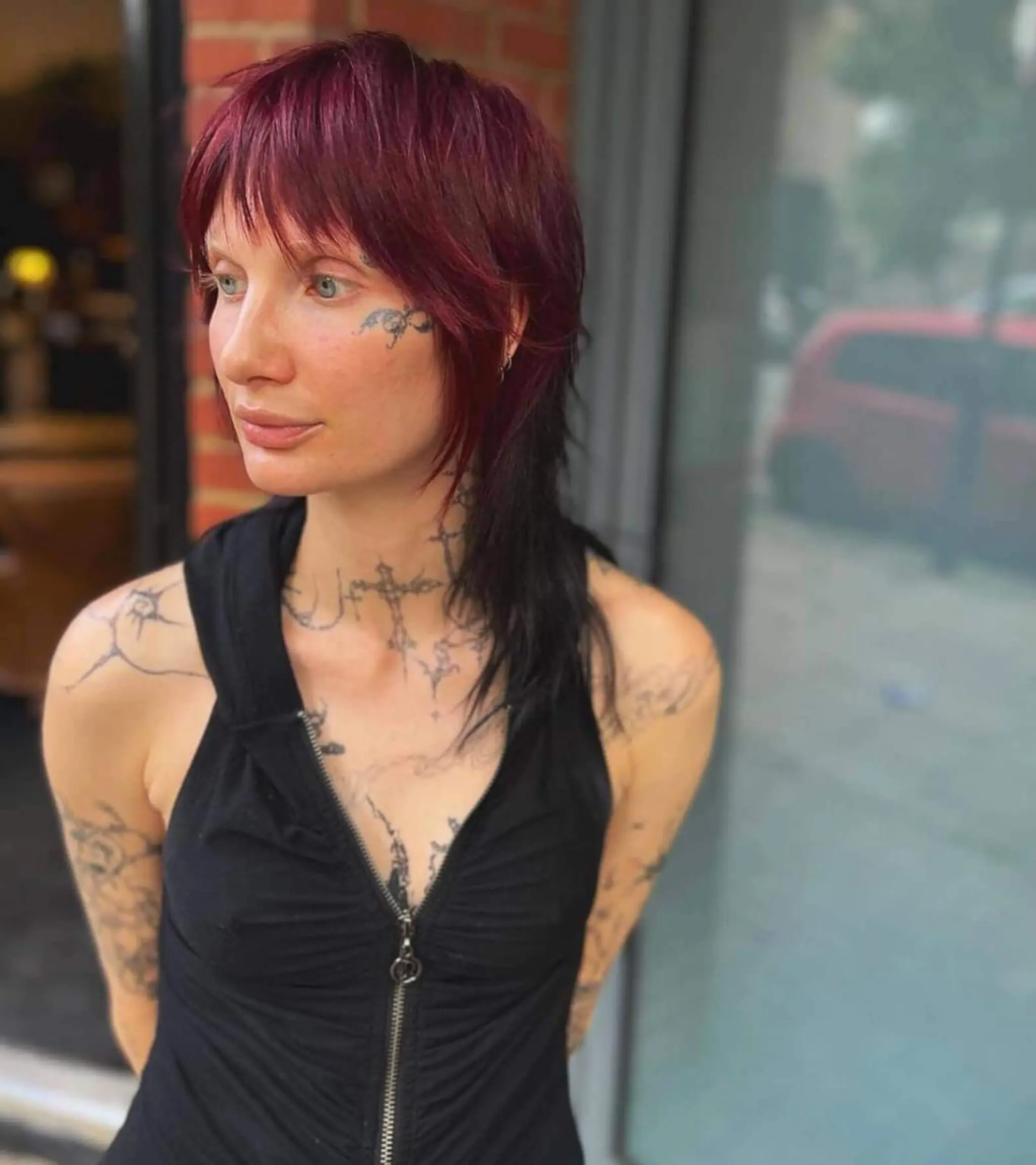 An edgy, layered medium-length cut with vibrant red shades at the top, blending into jet black at the ends, complete with fringe bangs.