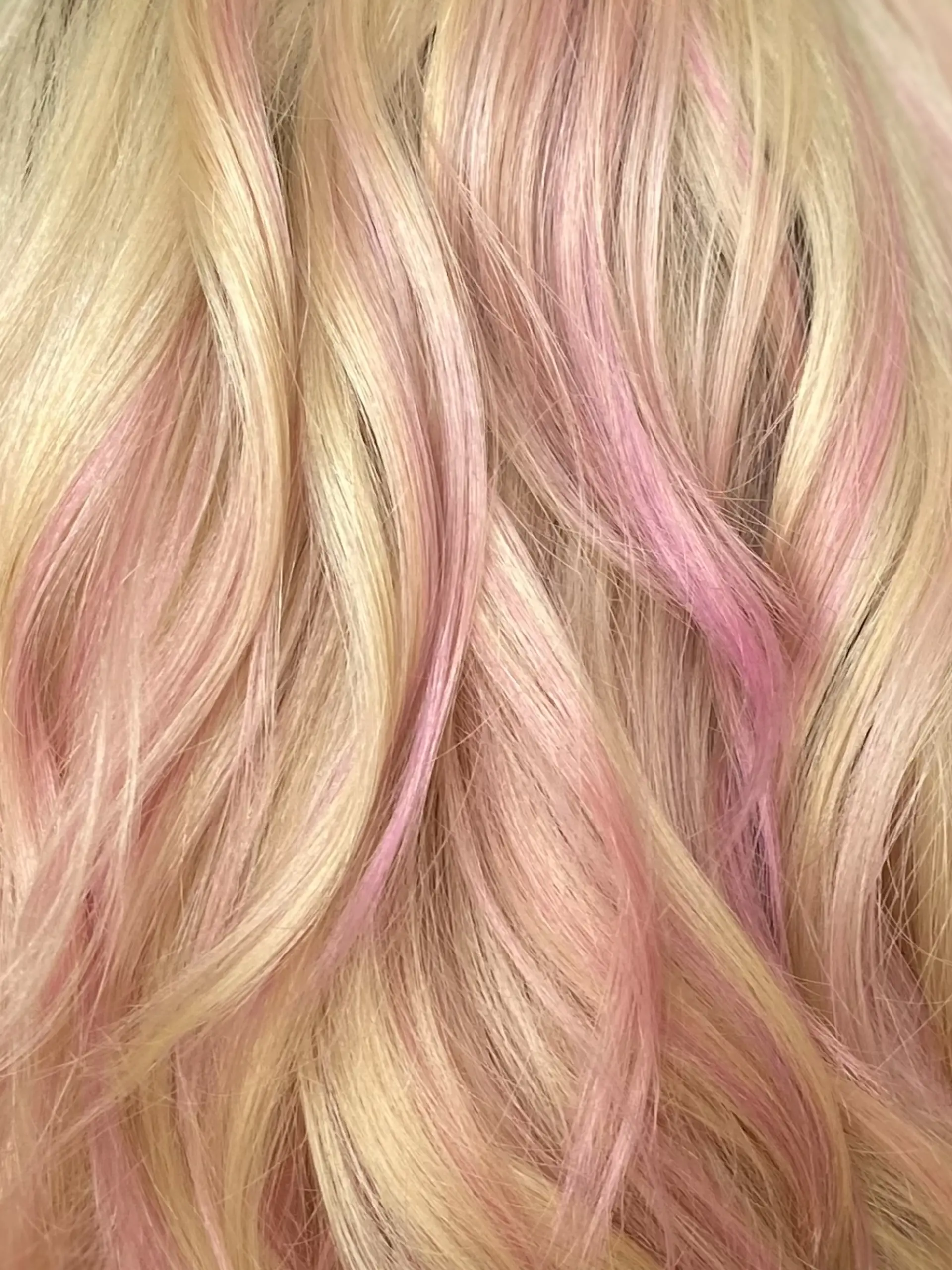 Close-up of soft wavy blonde hair woven with delicate pastel pink and blush ribbons of color. 1