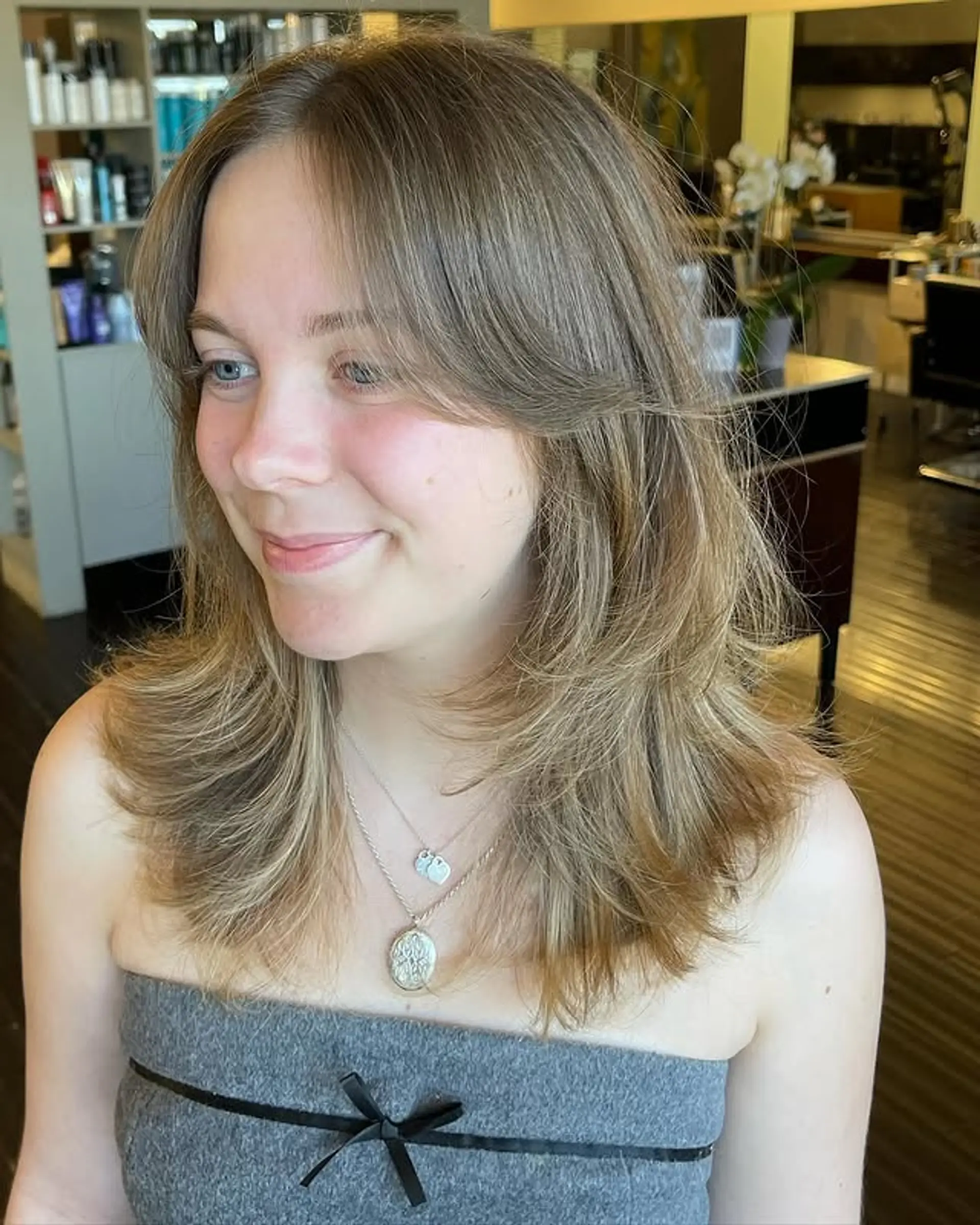 A medium length layered haircut with face-framing curtain bangs. 1