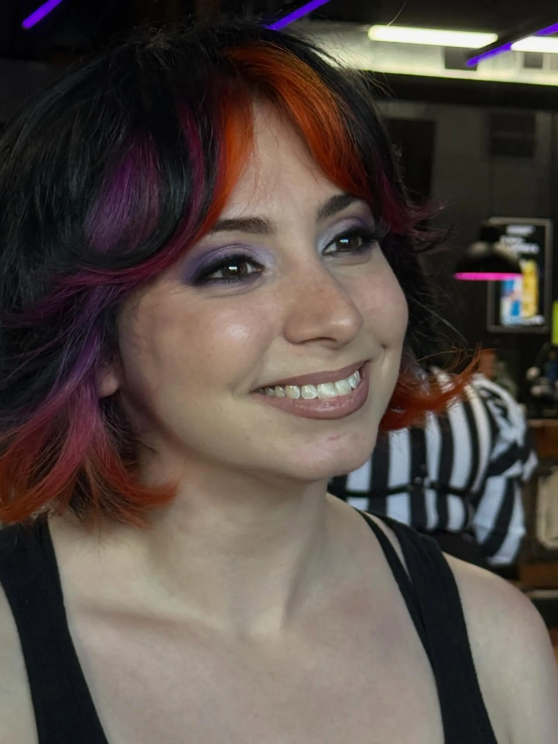 A textured layered bob featuring curtain bangs with vivid orange, purple, and magenta face-framing color accents on a dark base. 1