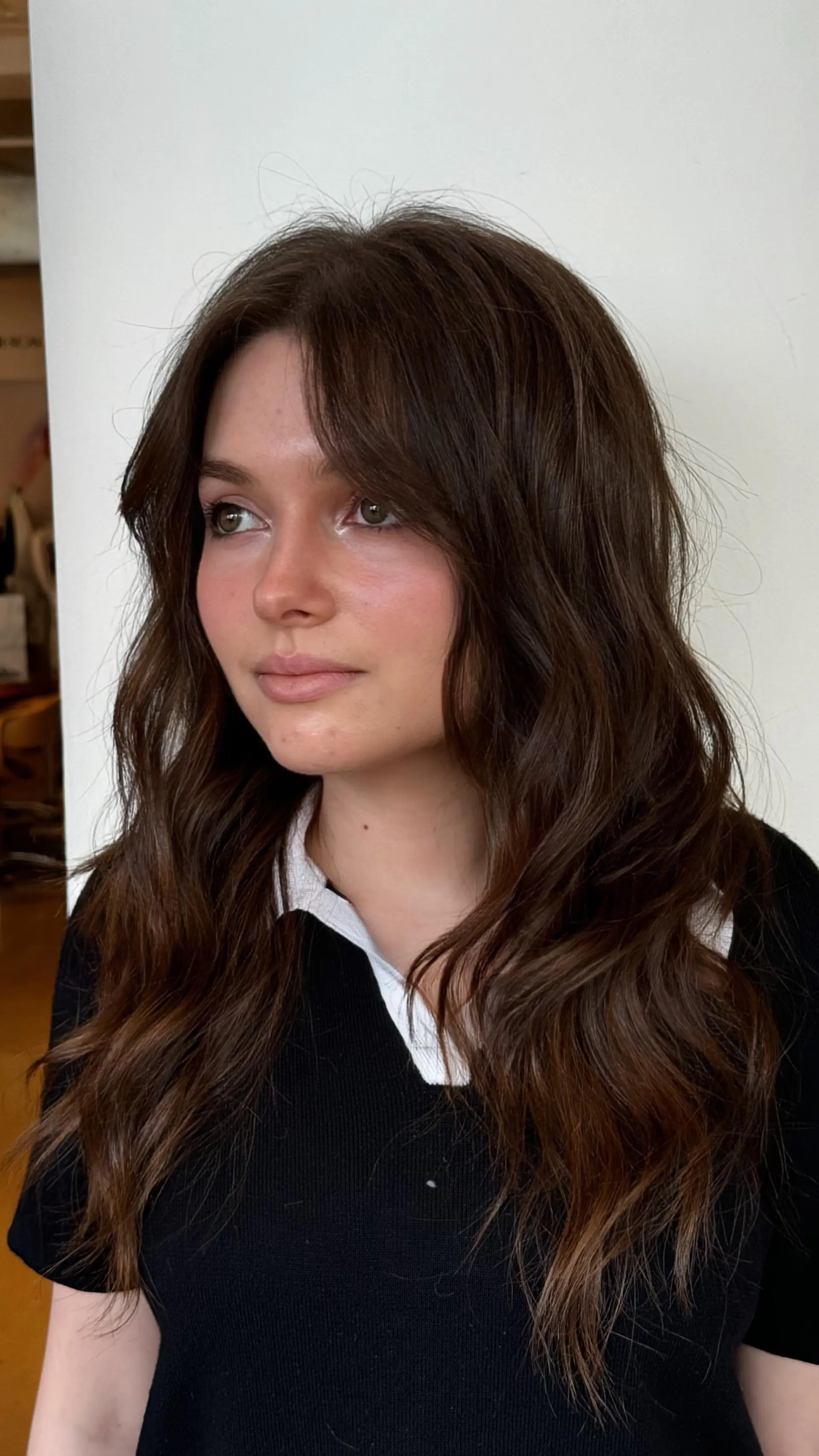 Long dark brown hair cut with textured, face-framing curtain bangs and styled in loose, tousled waves. 1