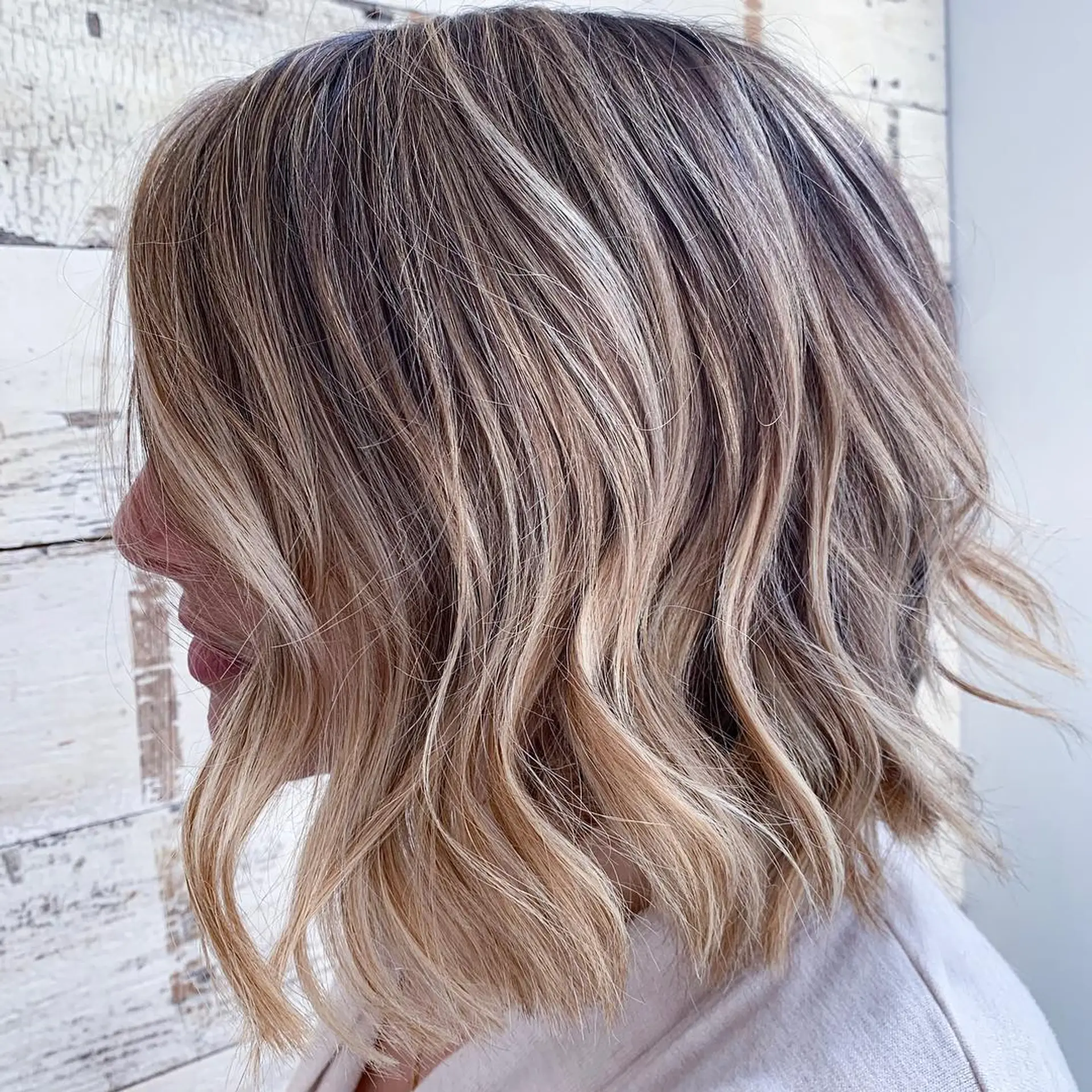 A textured, collarbone-grazing bob styled with soft, loose waves and multi-dimensional blonde balayage highlights. 1