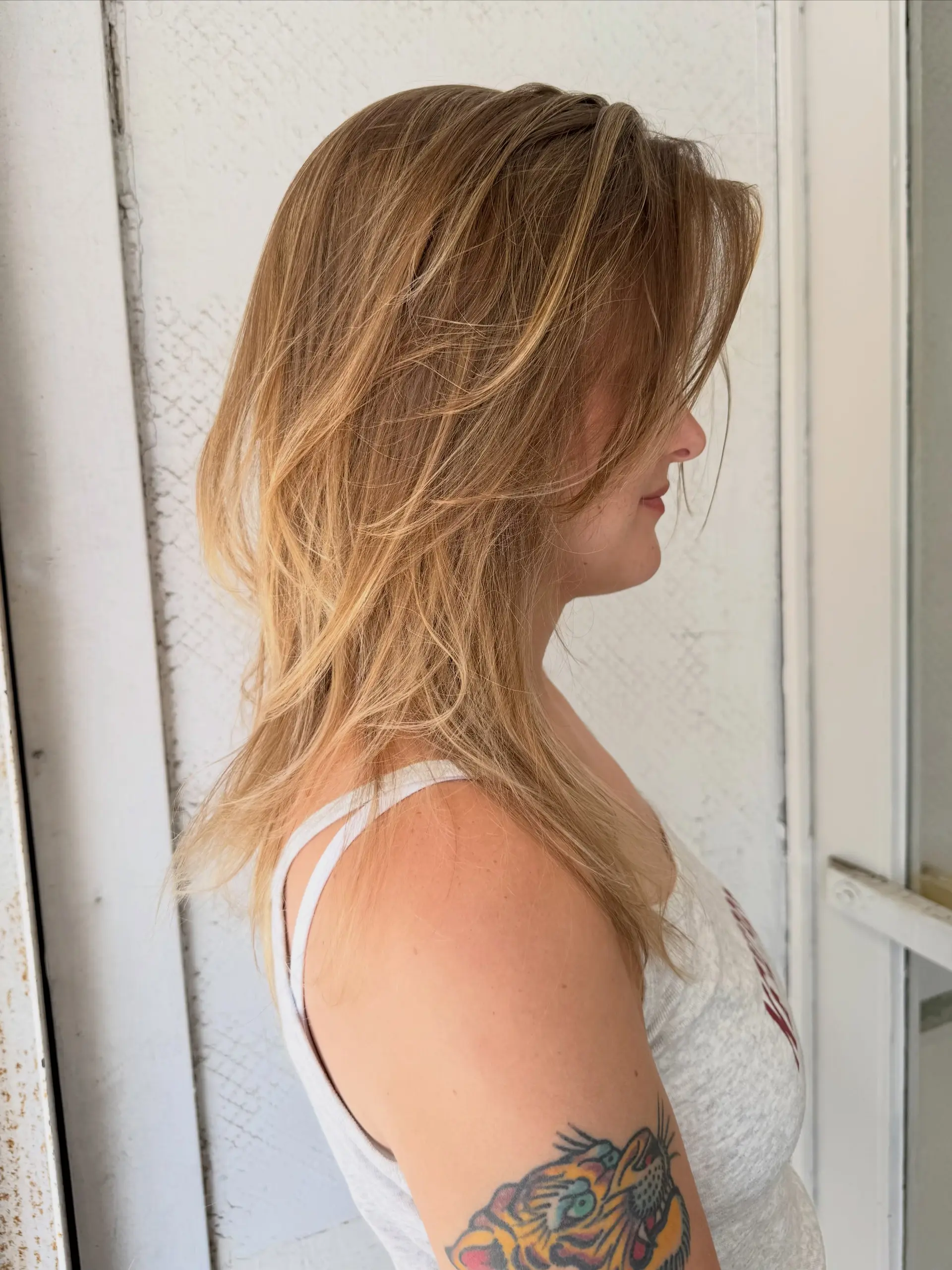 Medium-length warm honey blonde hair styled with soft, feathery layers and seamless airtouch balayage highlights. 1