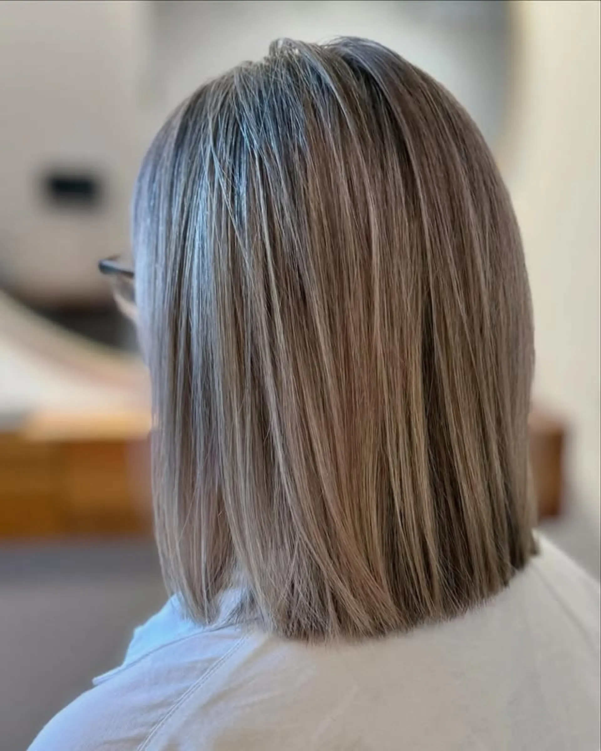 A sleek, blunt-cut bob featuring dimensional ash blonde highlights and subtle natural roots, offering a polished and contemporary finish. 1