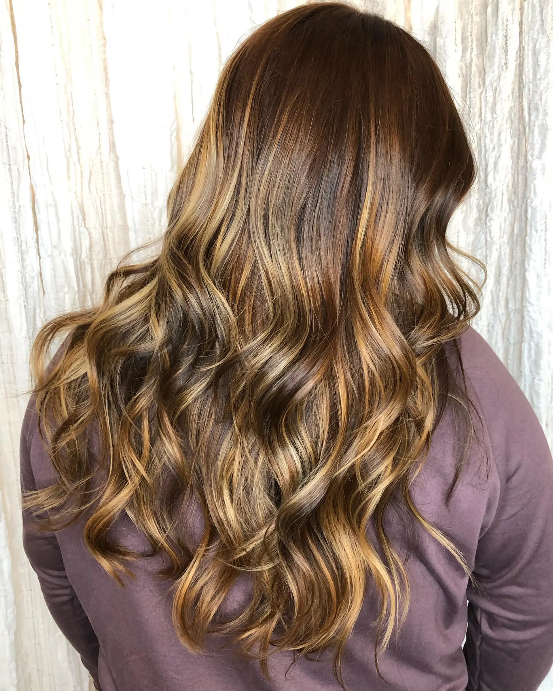 Long hair styled in soft, flowing waves with a dimensional warm caramel and honey balayage over a deep brunette base. 1