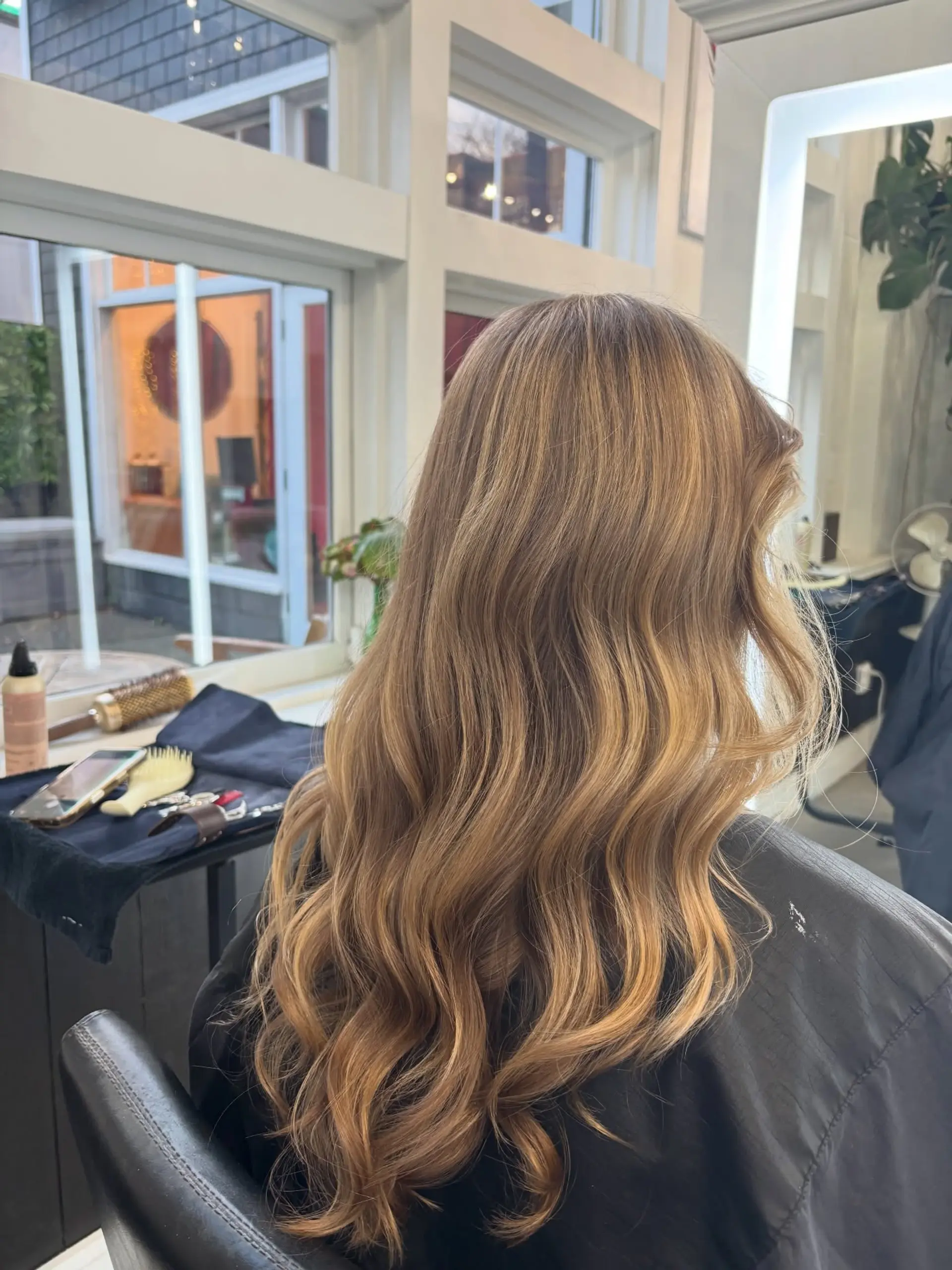 Long dimensional golden blonde hair styled into soft, bouncy waves with a radiant finish. 1