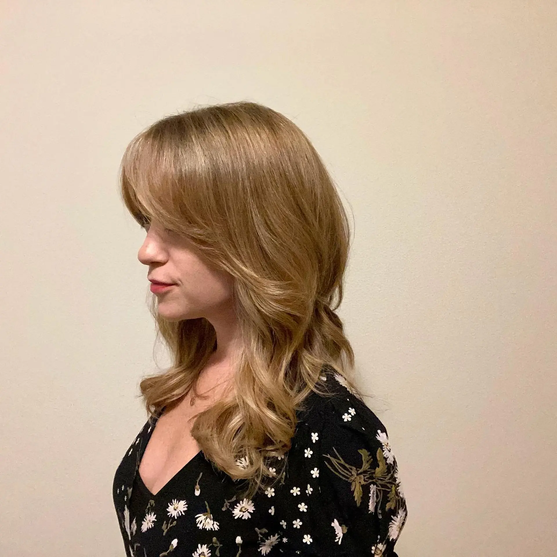 Medium-length warm blonde hair with feathered curtain bangs and soft, voluminous waves. 1