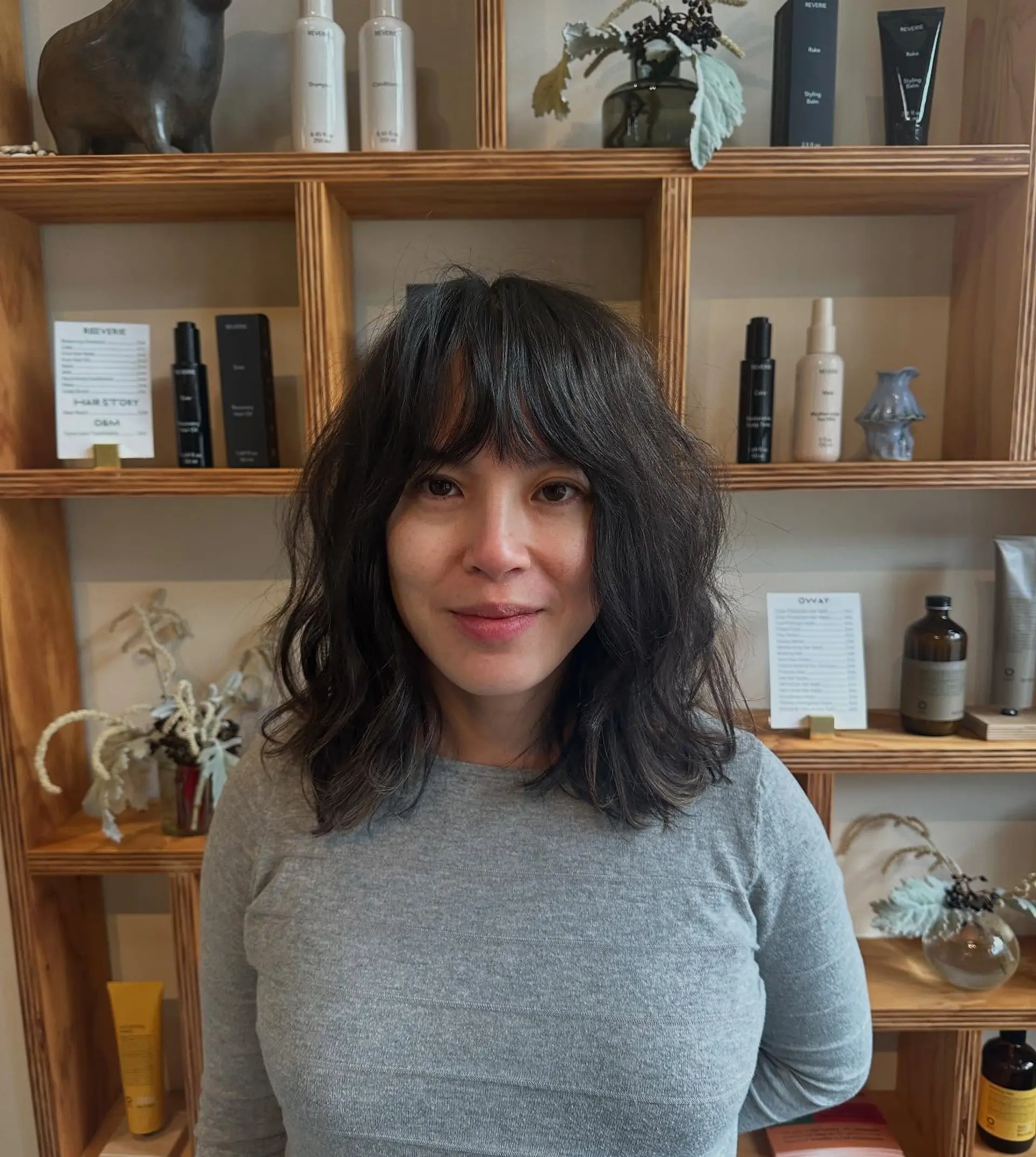 A shoulder-length wavy haircut featuring textured layers and full wispy bangs framing the face. 1